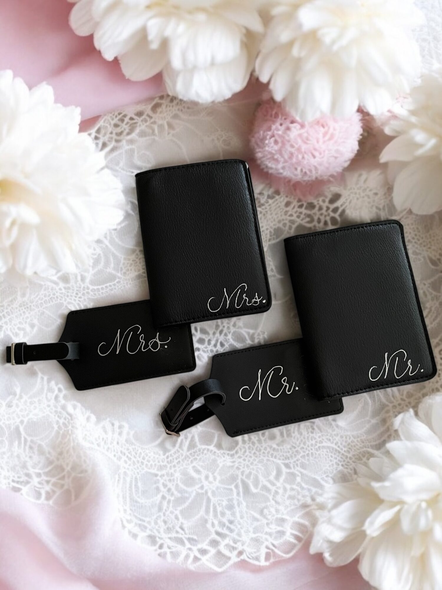 Four black luggage tags with white cursive text reading 'Mrs.' and 'Mr.' on lace and floral background.