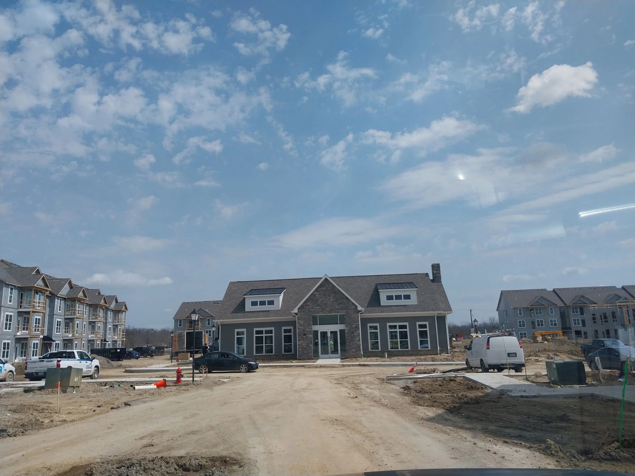 Construction site with a large building, surrounded by dirt roads and parked vehicles, under a partly cloudy sky.