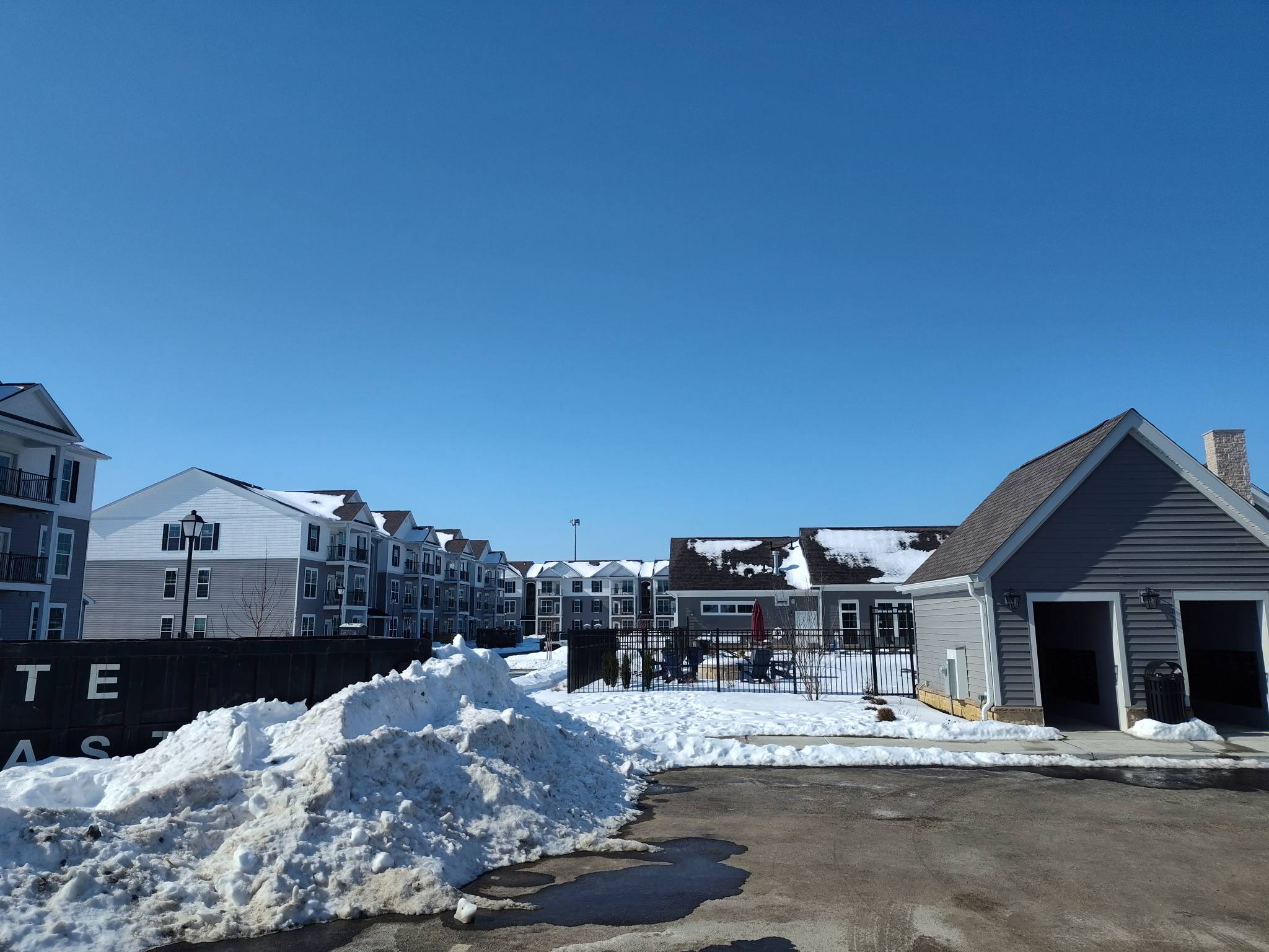 Snow-covered ground with buildings and a garage under a clear blue sky.