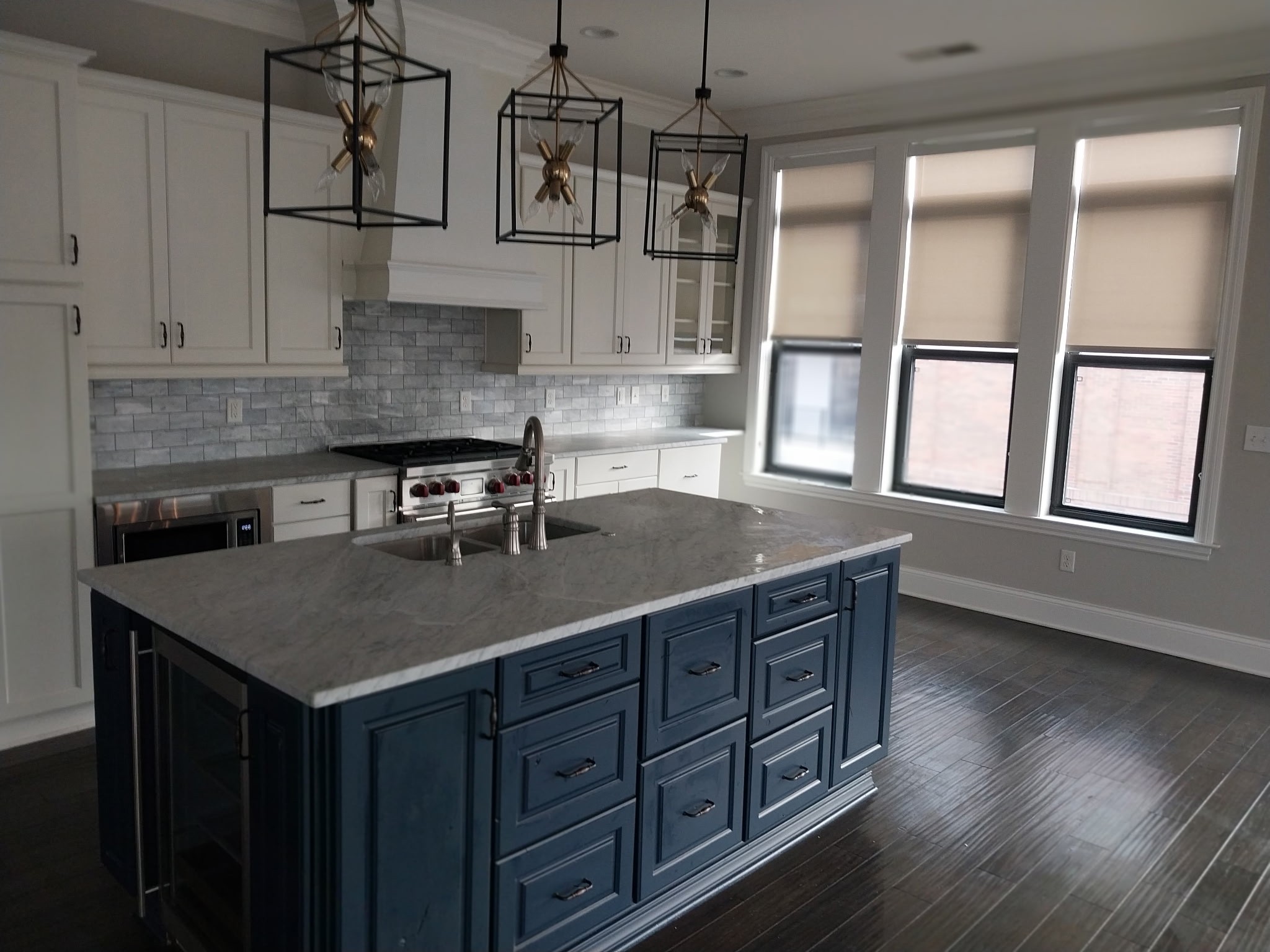 Modern kitchen with white cabinets, gray backsplash, blue island, and three pendant lights with star-shaped decorations.