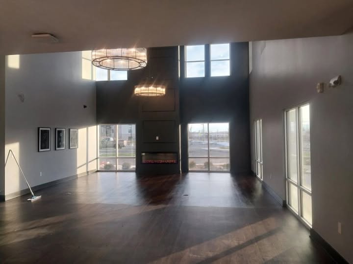 Empty room with large windows, hardwood floor, and a fireplace, illuminated by natural light.