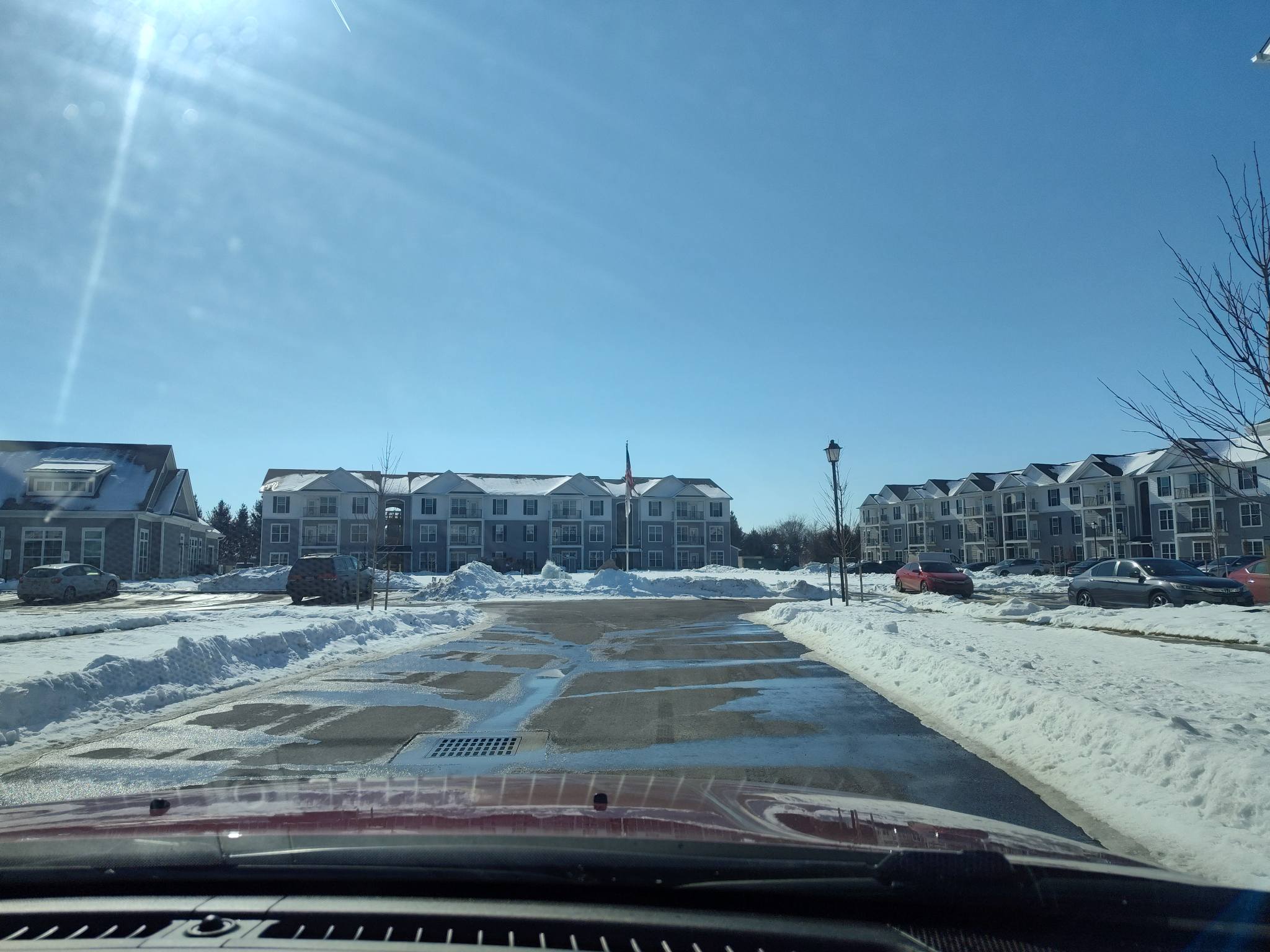 View of a snow-covered parking lot and residential buildings under a clear blue sky.