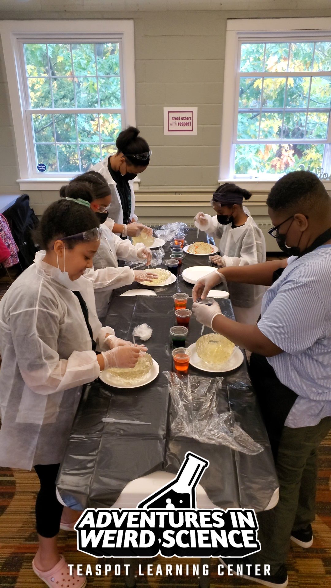Group of children and an adult in a classroom preparing food at a table with ingredients and utensils.