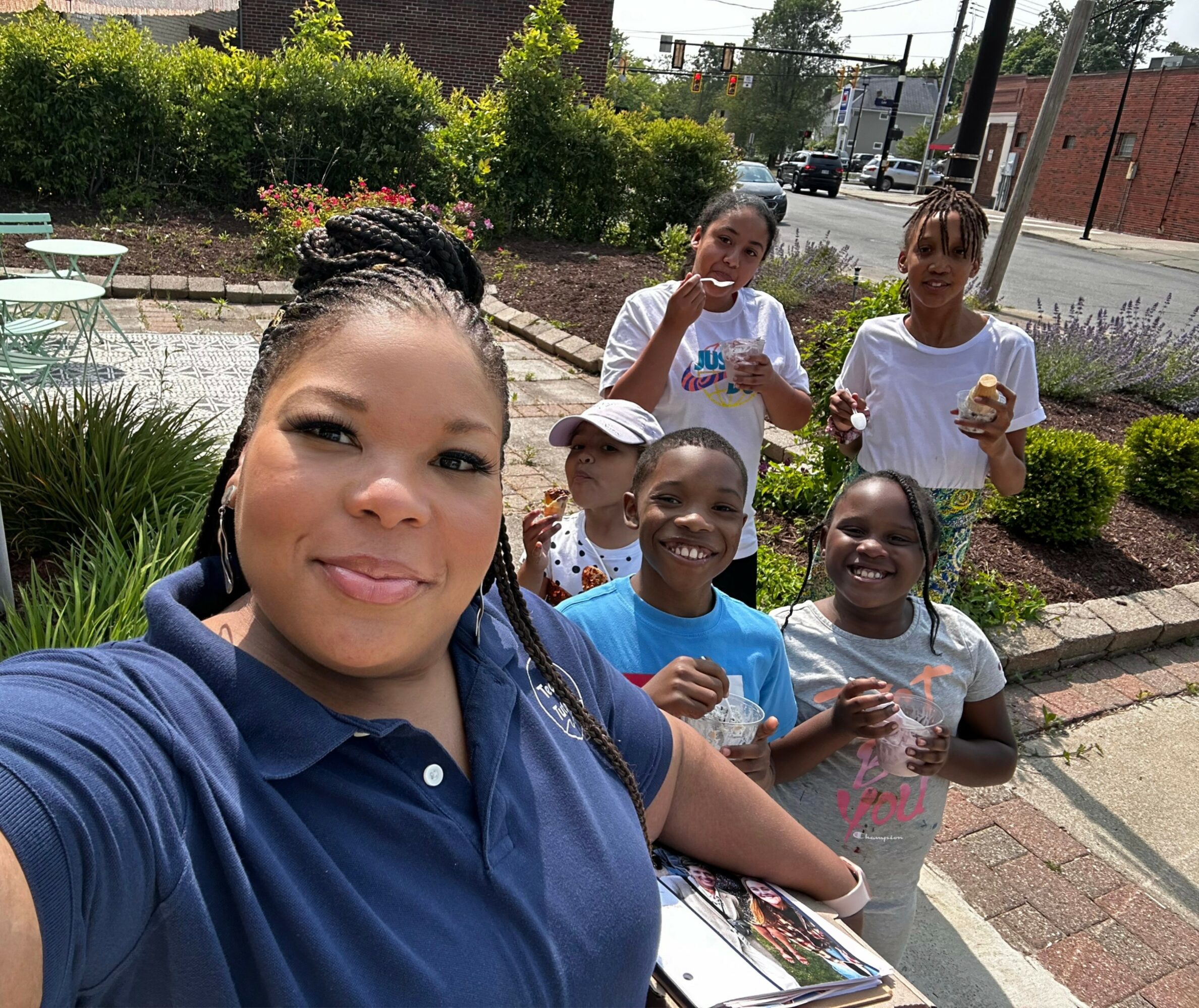Woman taking selfie with five children outdoors in a garden area, smiling and holding a book.