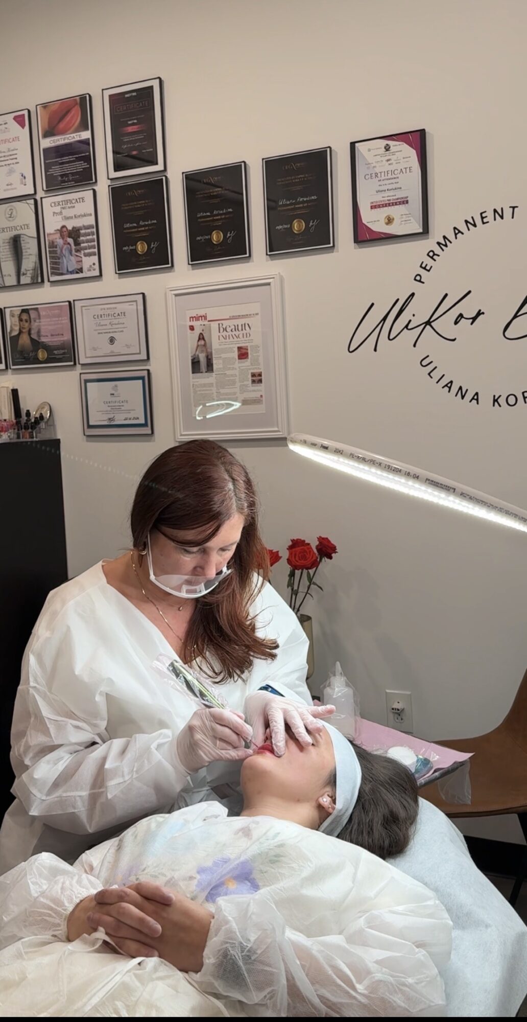 A woman in medical attire performs a facial treatment on a patient lying down with a headband, in a clinic room.