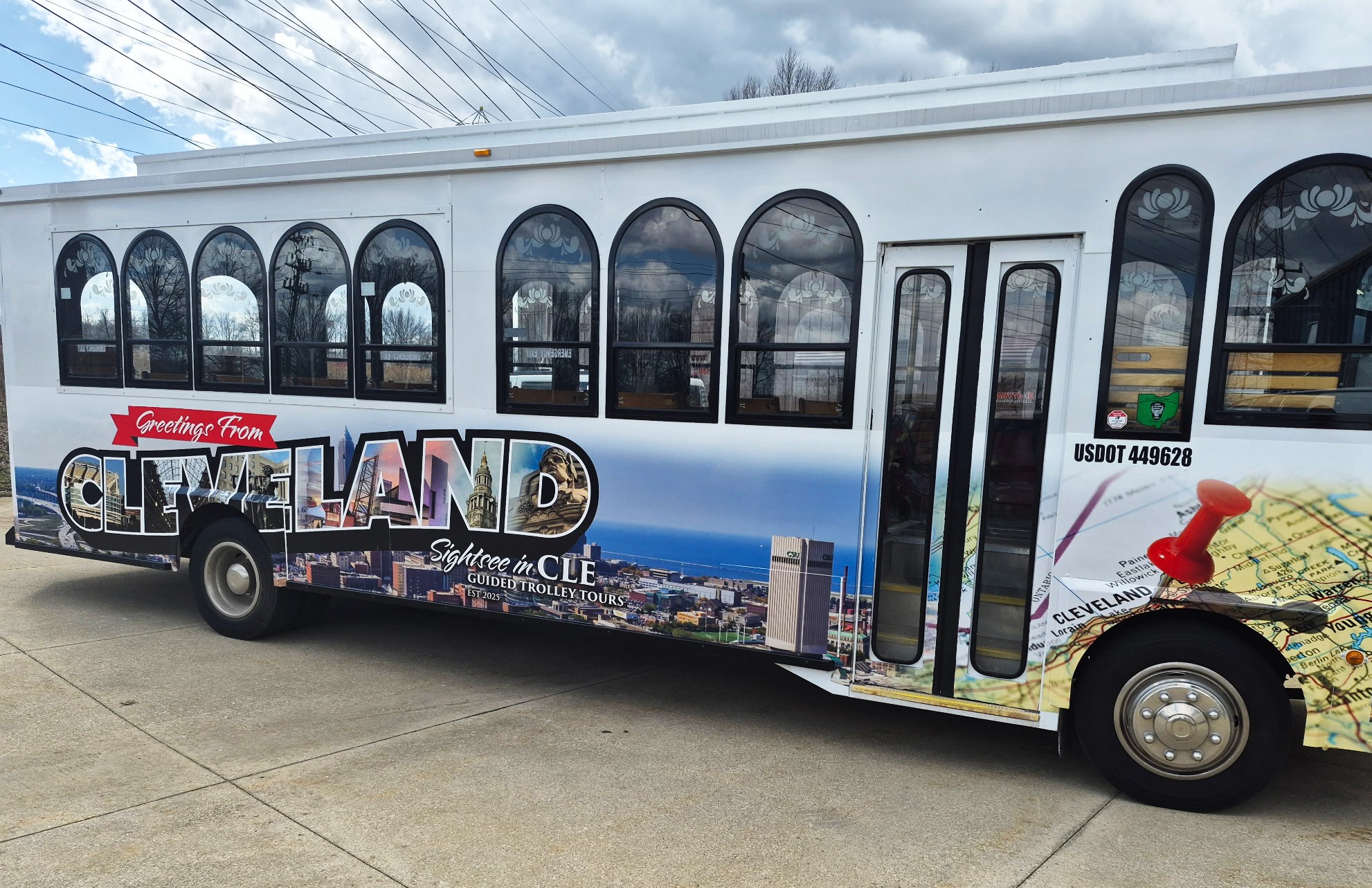Bus with large windows and colorful graphic design, including cityscape and map elements, parked on a street.