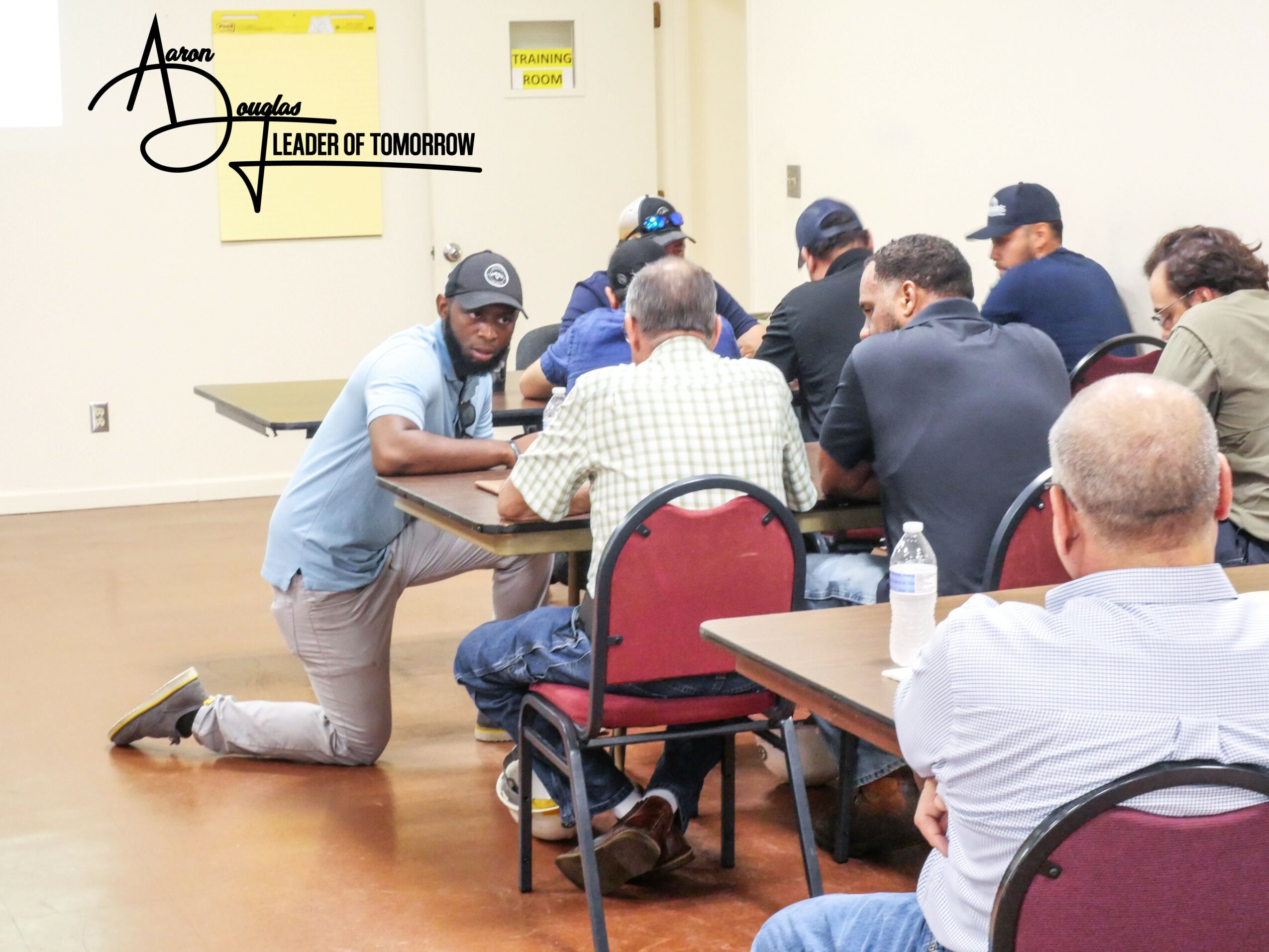Group of people seated around a table in a meeting room, some taking notes, others listening attentively.