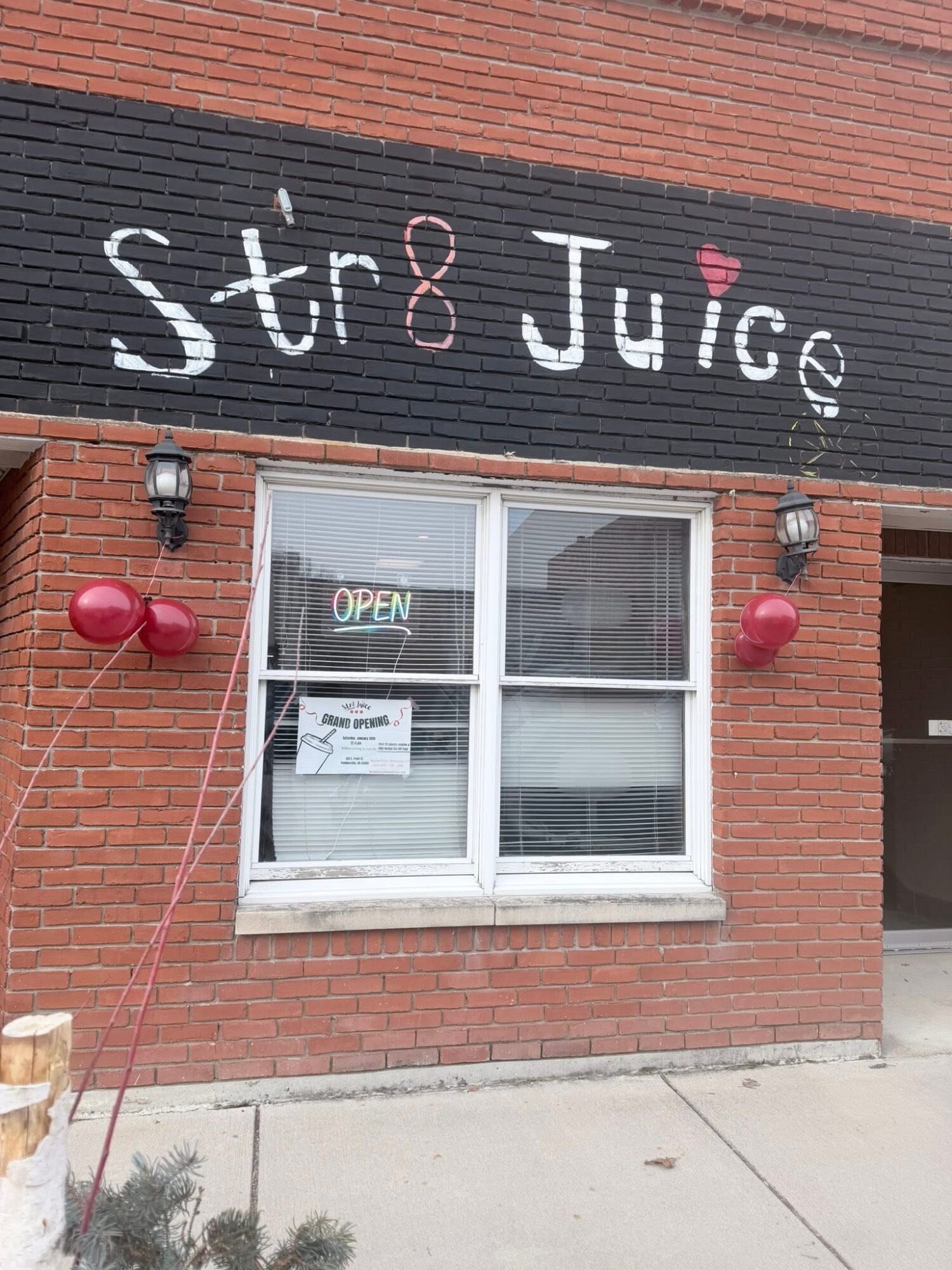 Brick building with a window and a sign that reads 'Str8 Juice' with a pink heart. Two red balloons are tied outside.