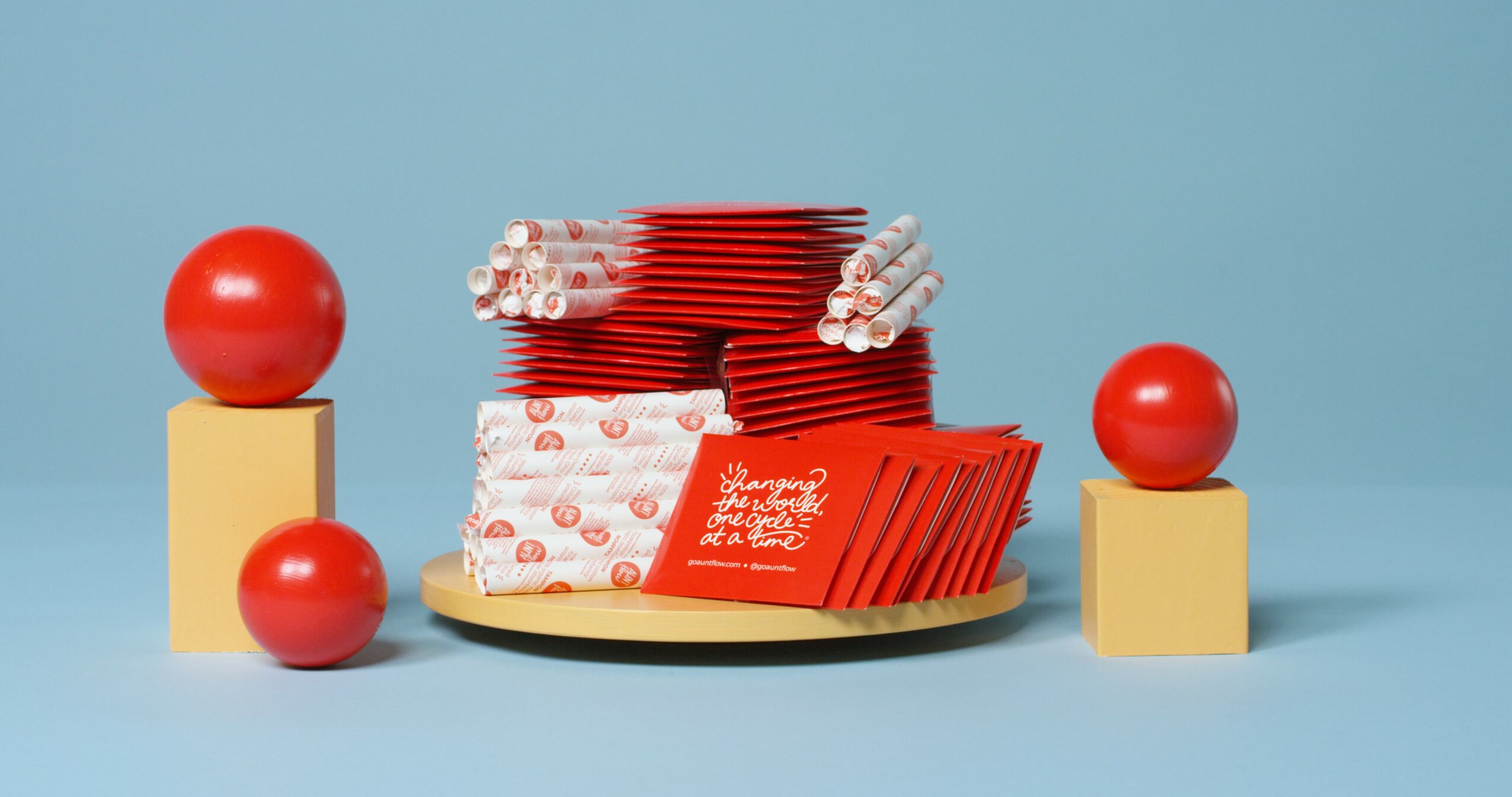 Stack of red and white wrapped candies on a round wooden tray with red balls on yellow blocks around it.
