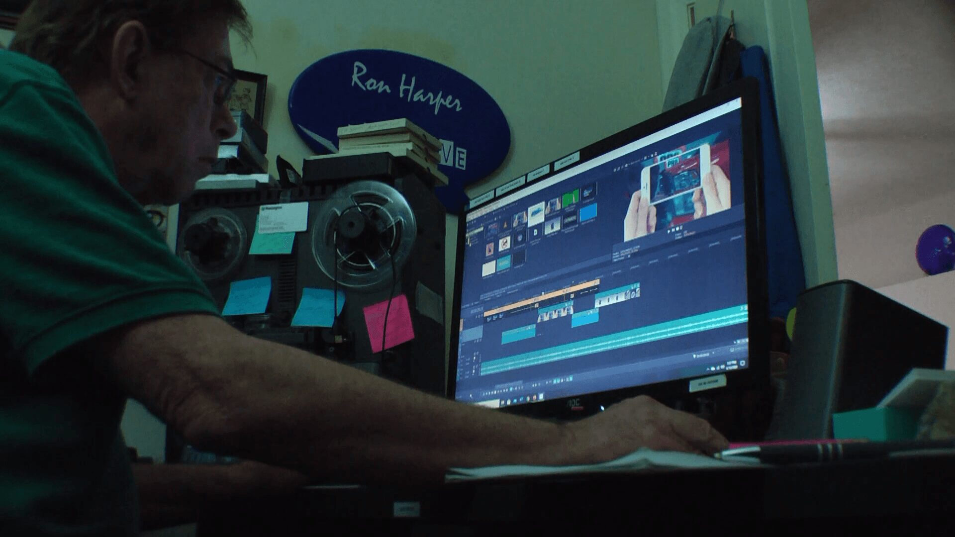 Person working at computer with video editing software open, in a room with a sign reading 'Ron Harper'.