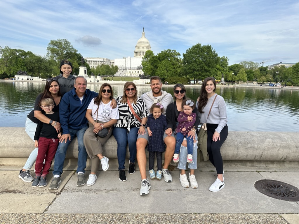 Group of ten people sitting on a stone ledge near a river with the Capitol building in the background.