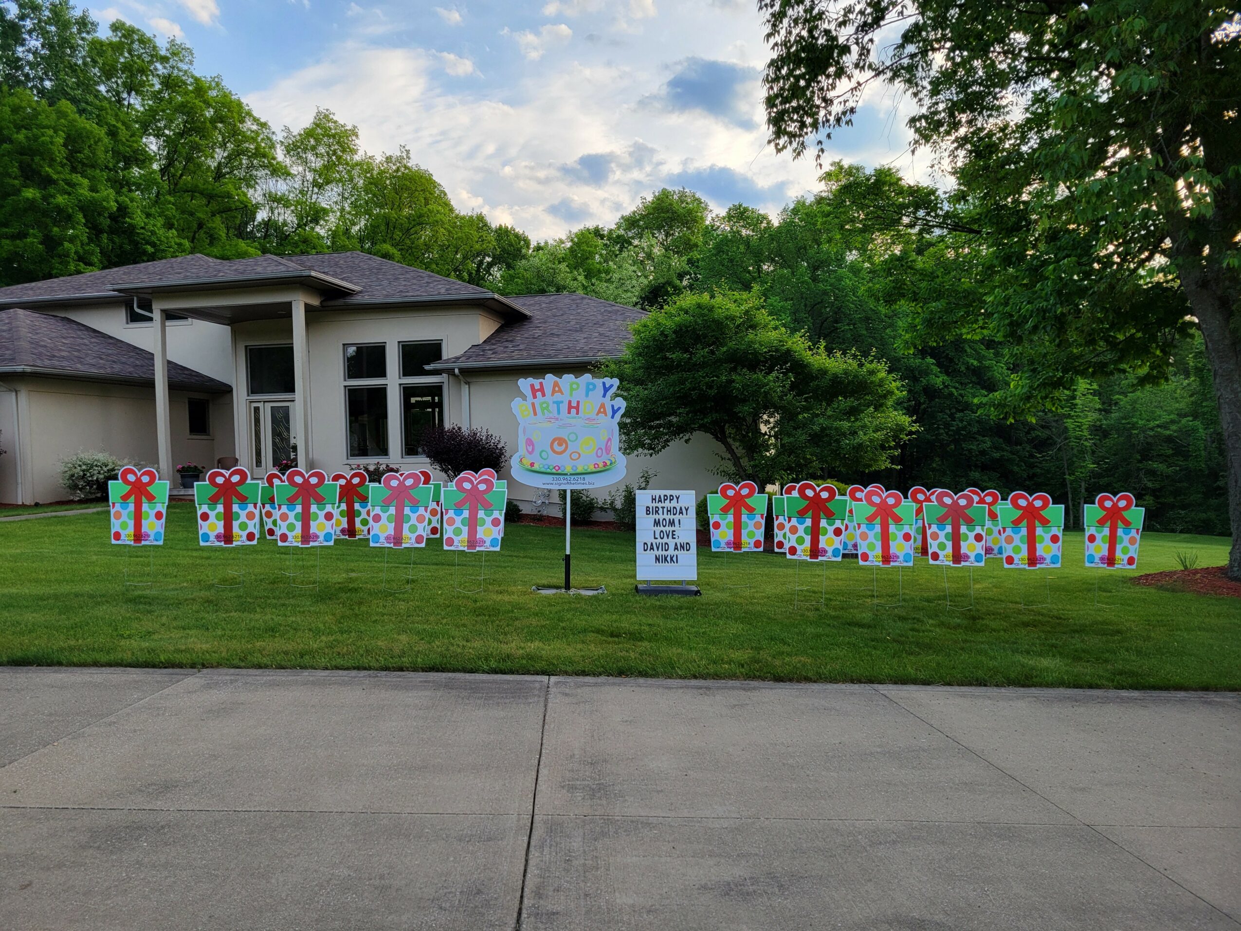 House with decorated lawn, sign, and trees in background, under partly cloudy sky.