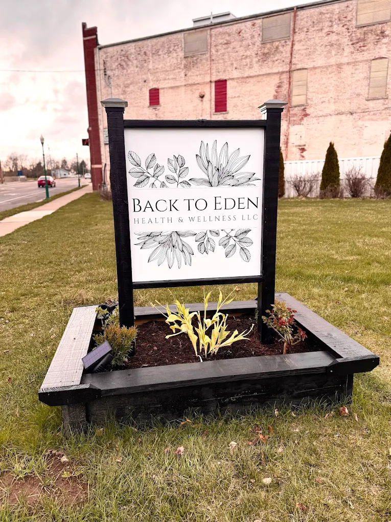 Signboard with floral design and text 'Back to Eden' in a garden bed outside a building.