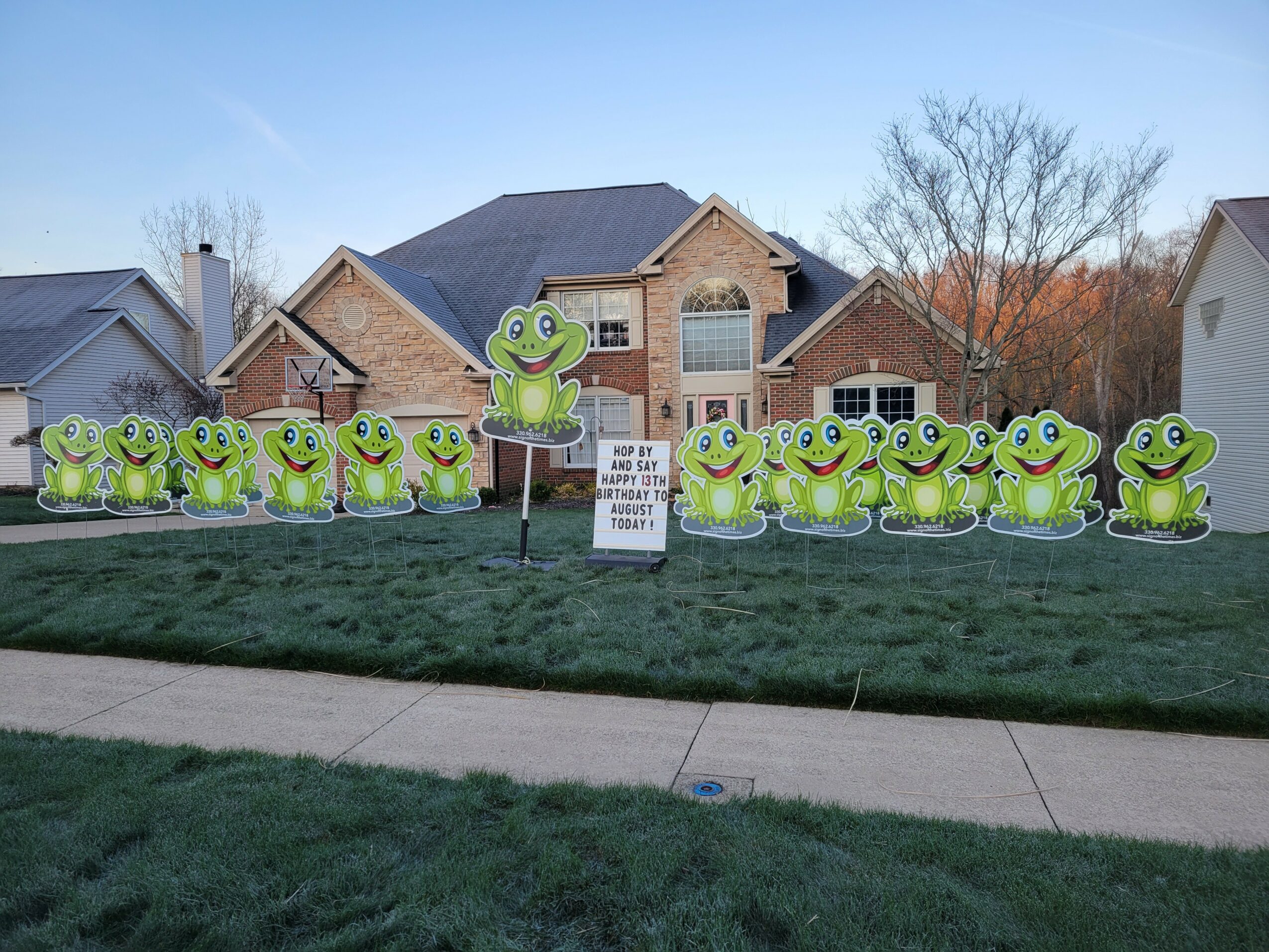 Multiple frog-shaped yard signs in front of a house, with a sign in the middle, on a grassy lawn.