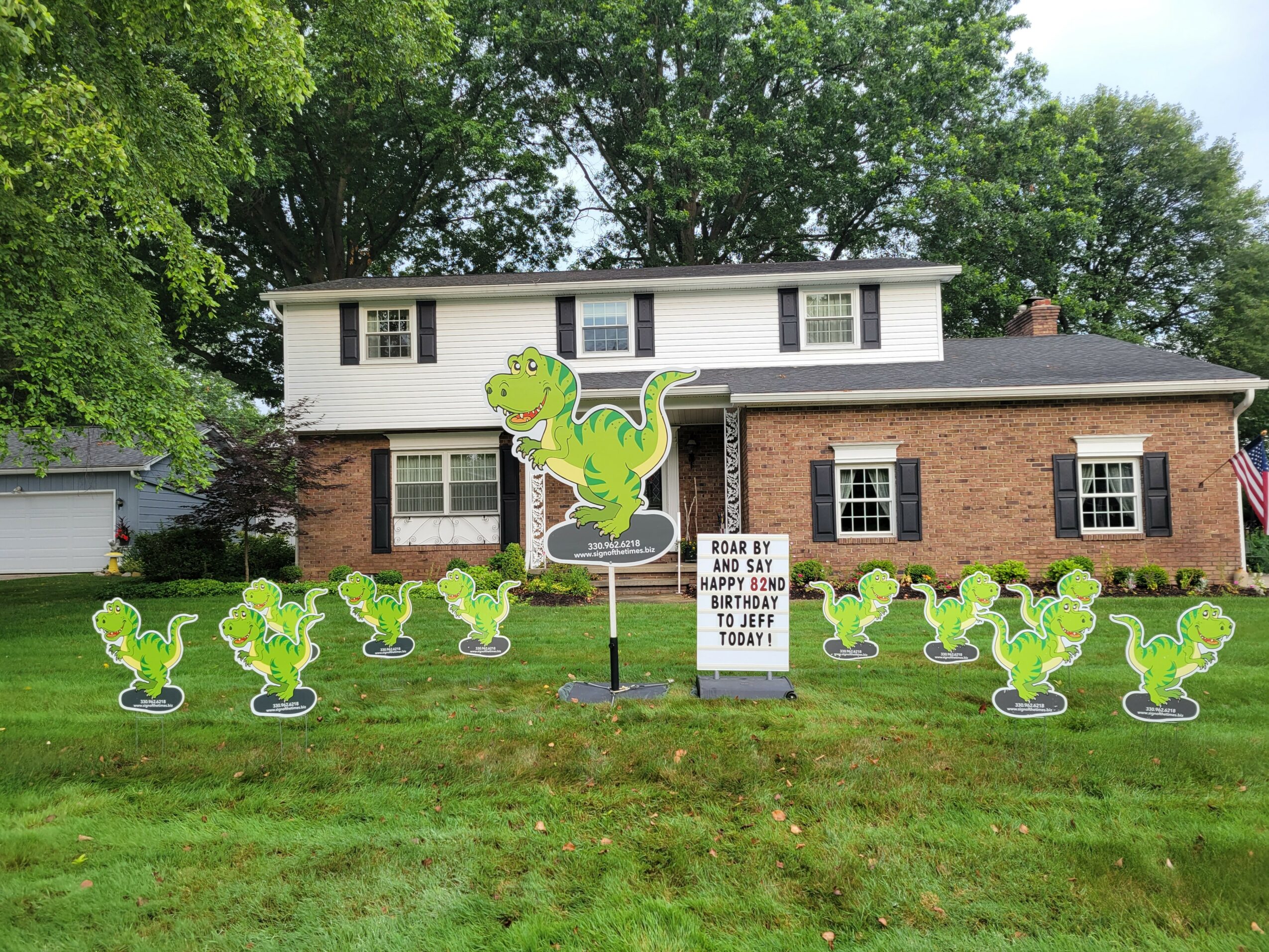 House with lawn decorated with multiple dinosaur cutouts and a sign in front.
