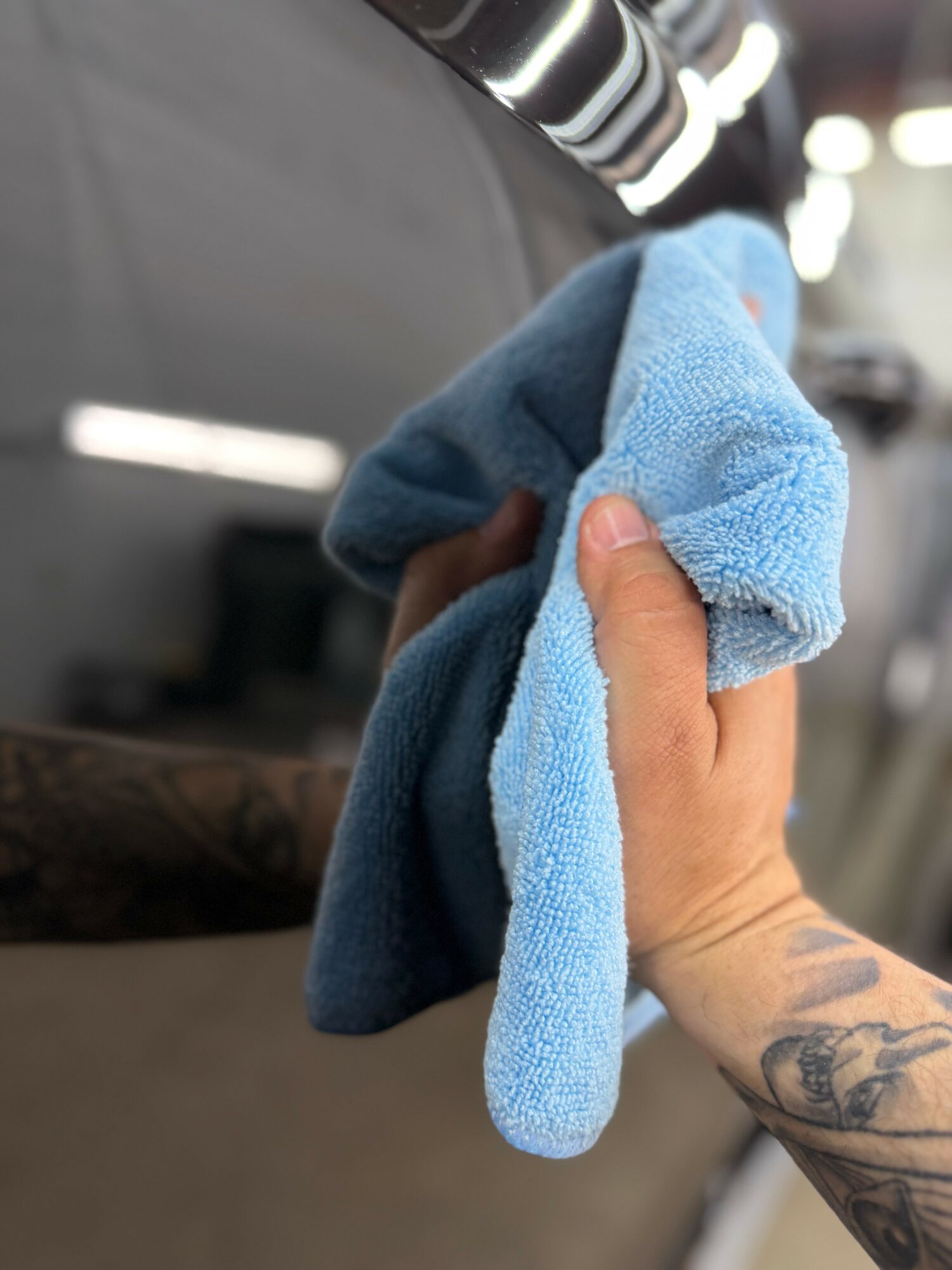 Person holding a blue microfiber cloth, wiping a dark surface in an indoor setting.