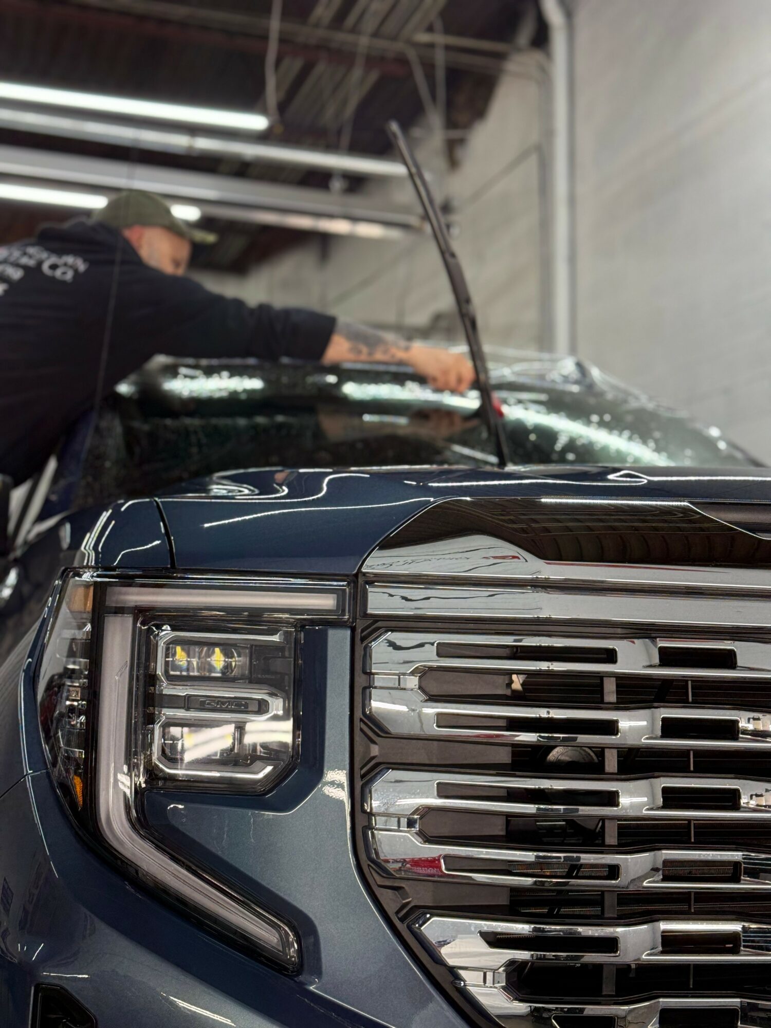 Person cleaning the front of a dark-colored vehicle inside a garage or workshop.