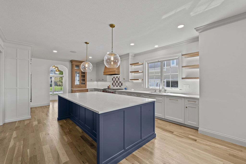 Modern kitchen with white cabinets, a large blue island, pendant lights, and wooden flooring.