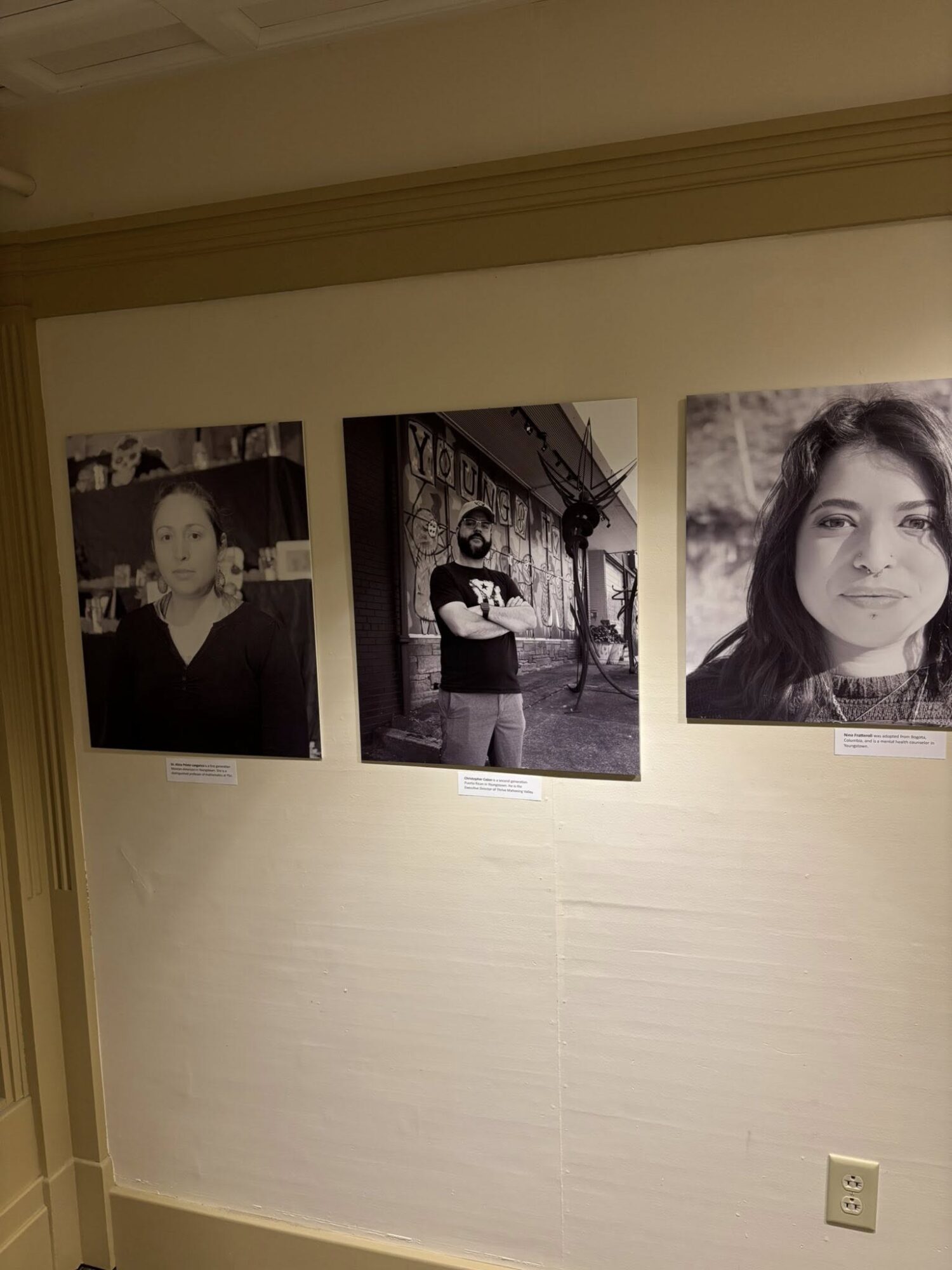 Three black and white photographs of people displayed on a wall, with labels beneath each photo.