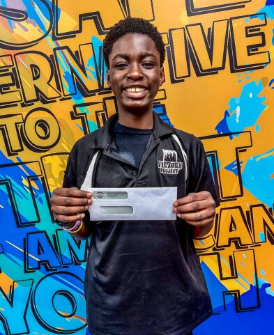 Young person smiling, holding a check, standing in front of a colorful background with text and graphics.