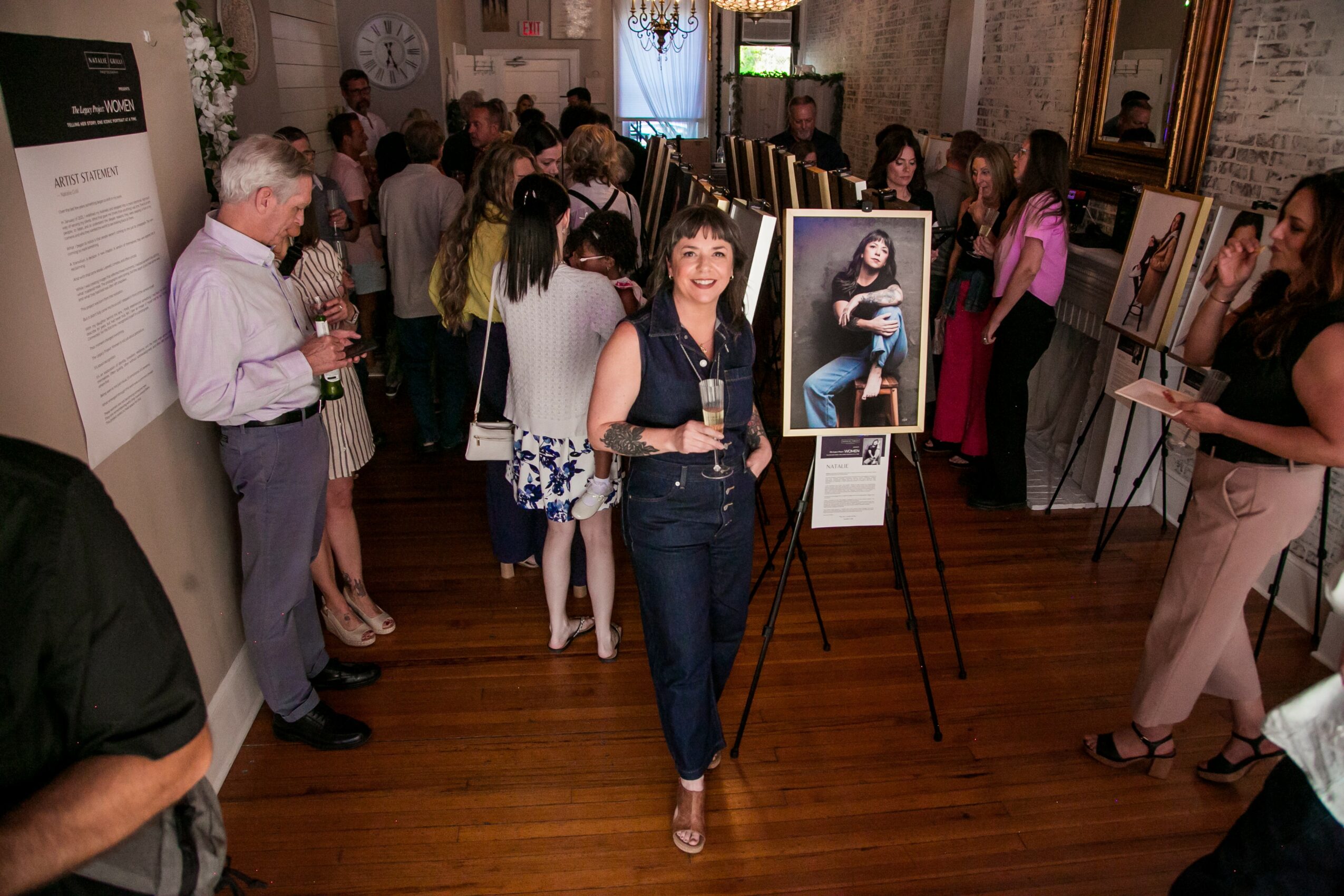 Gallery with people viewing photographs on display, some engaging in conversation, wooden floor, and framed pictures on walls.