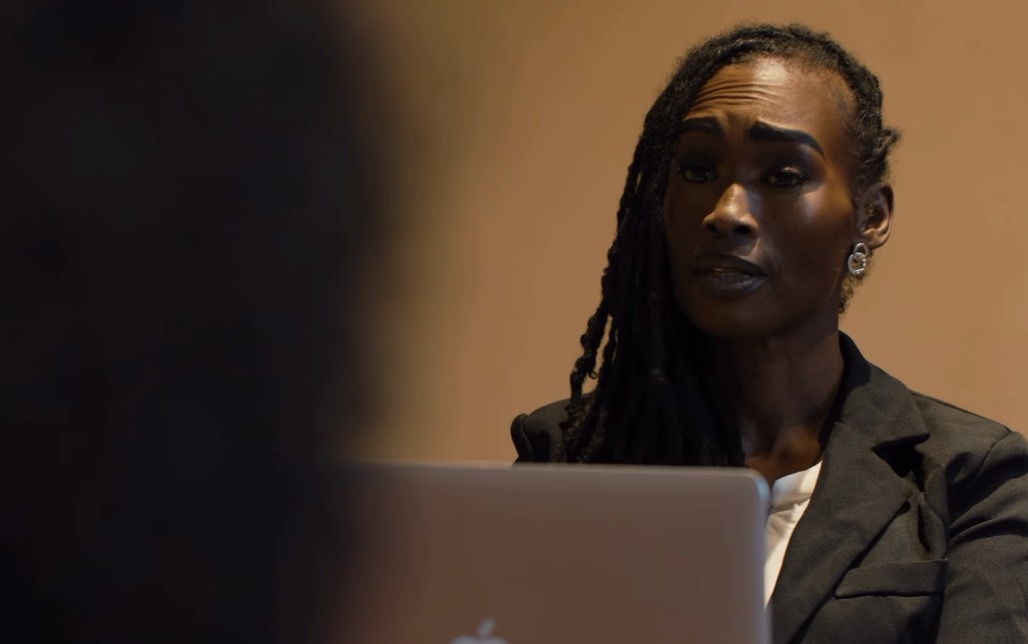 Woman with dreadlocks looking at a laptop screen, with a blurred person in the foreground.