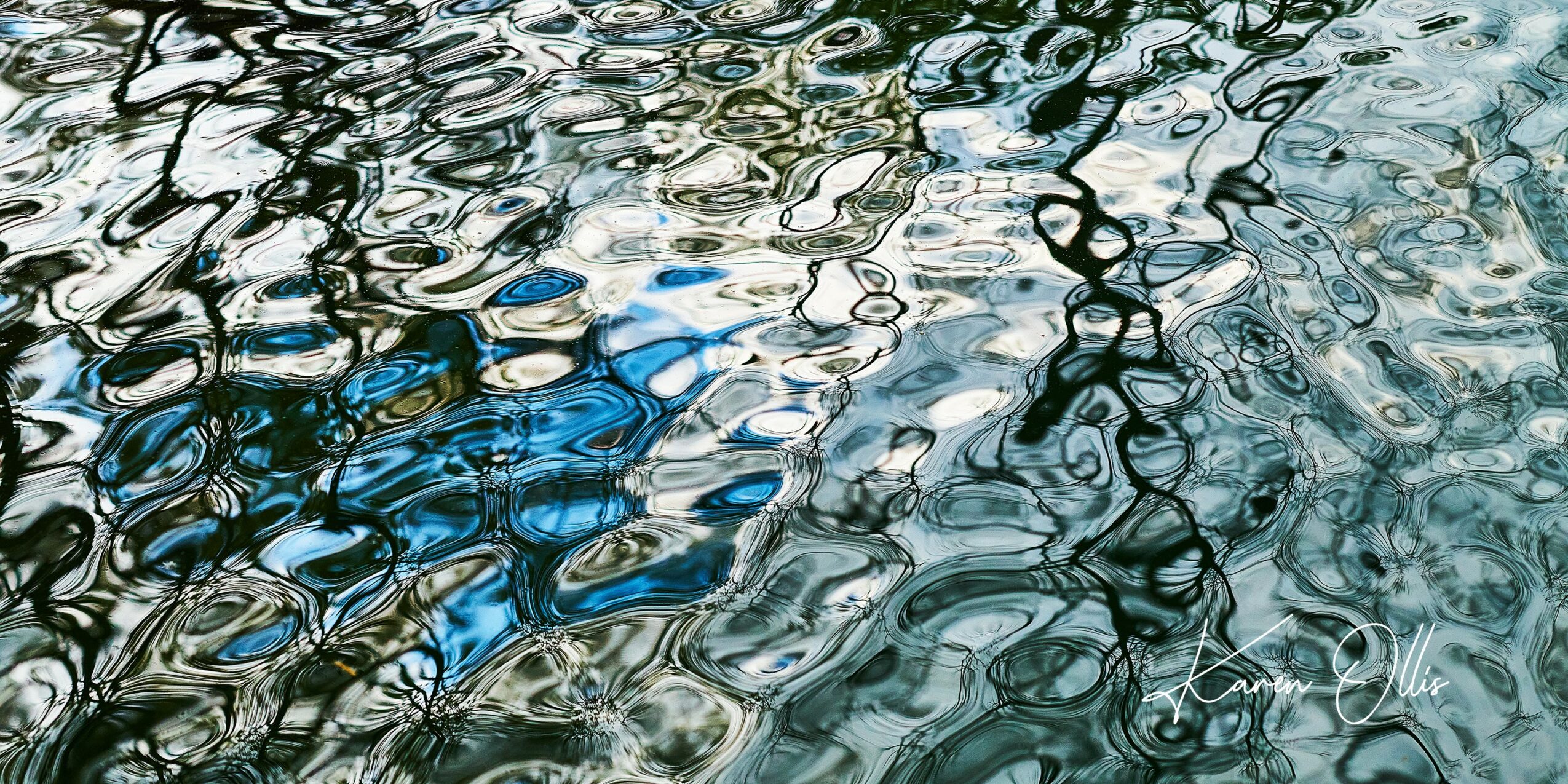 Reflections on water with ripples creating abstract patterns in various shades of blue, gray, and black.