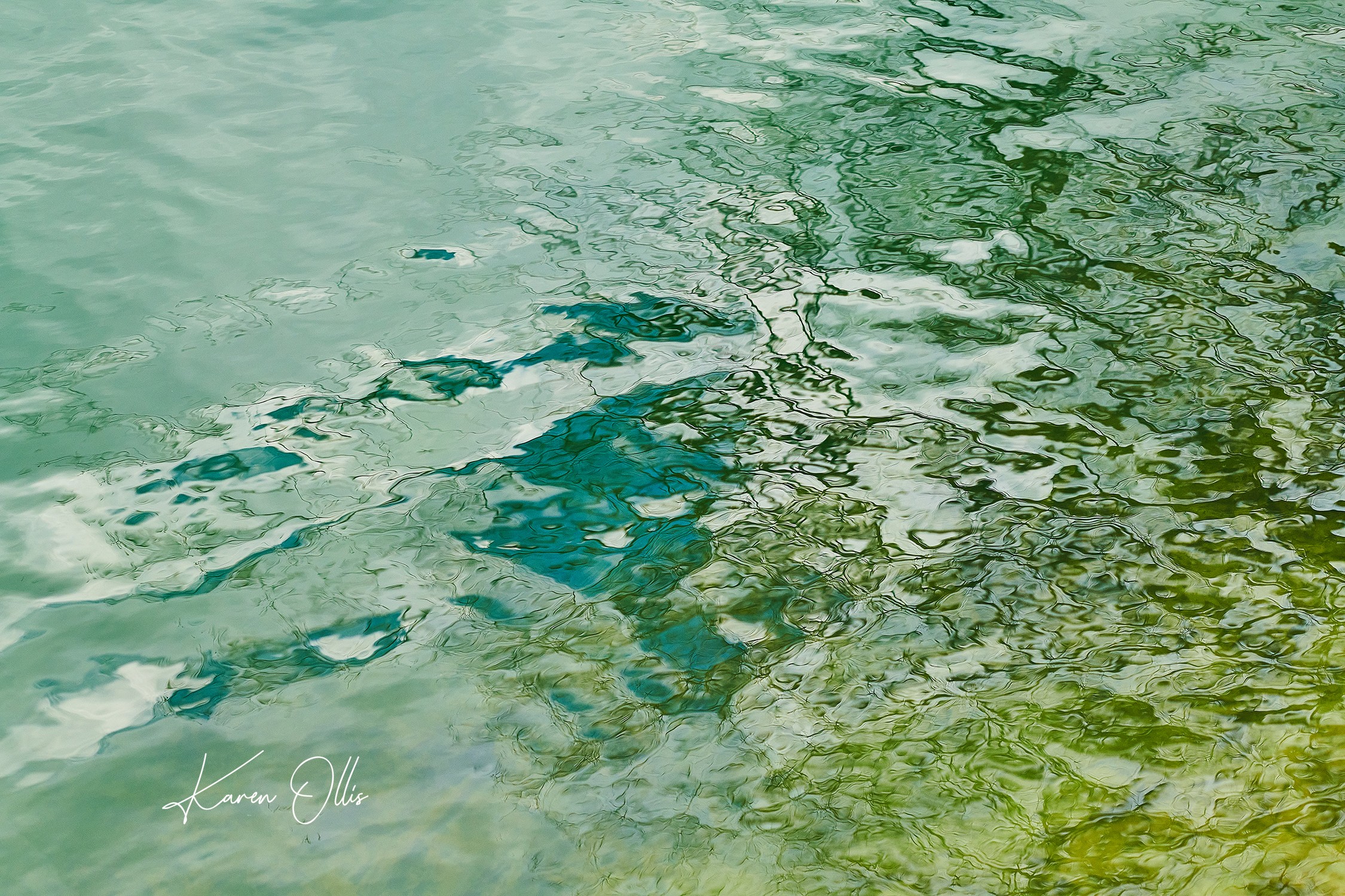 Water surface with reflections and ripples, showing green and blue hues.
