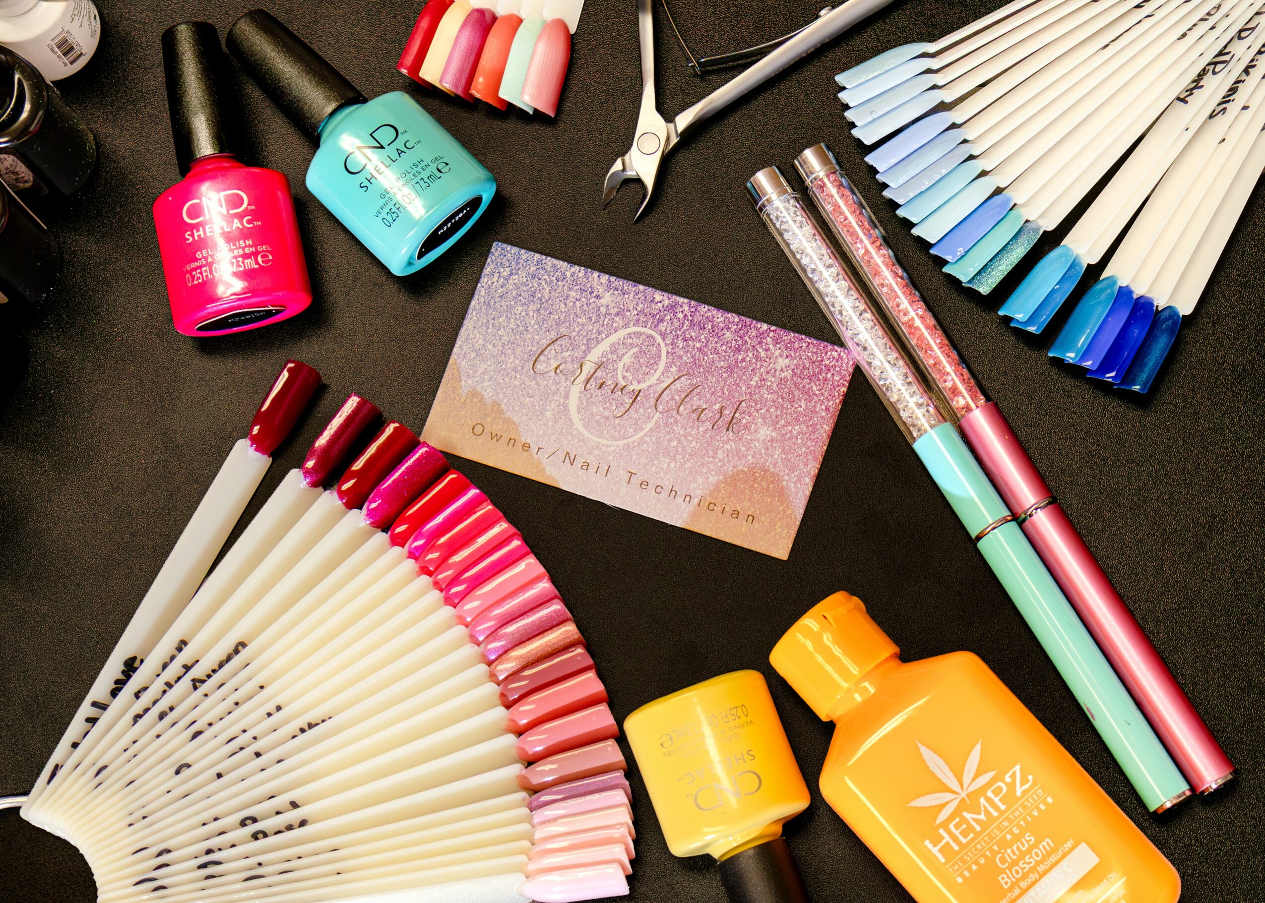 Nail polish bottles, fan of nail color samples, and a business card on a black surface.