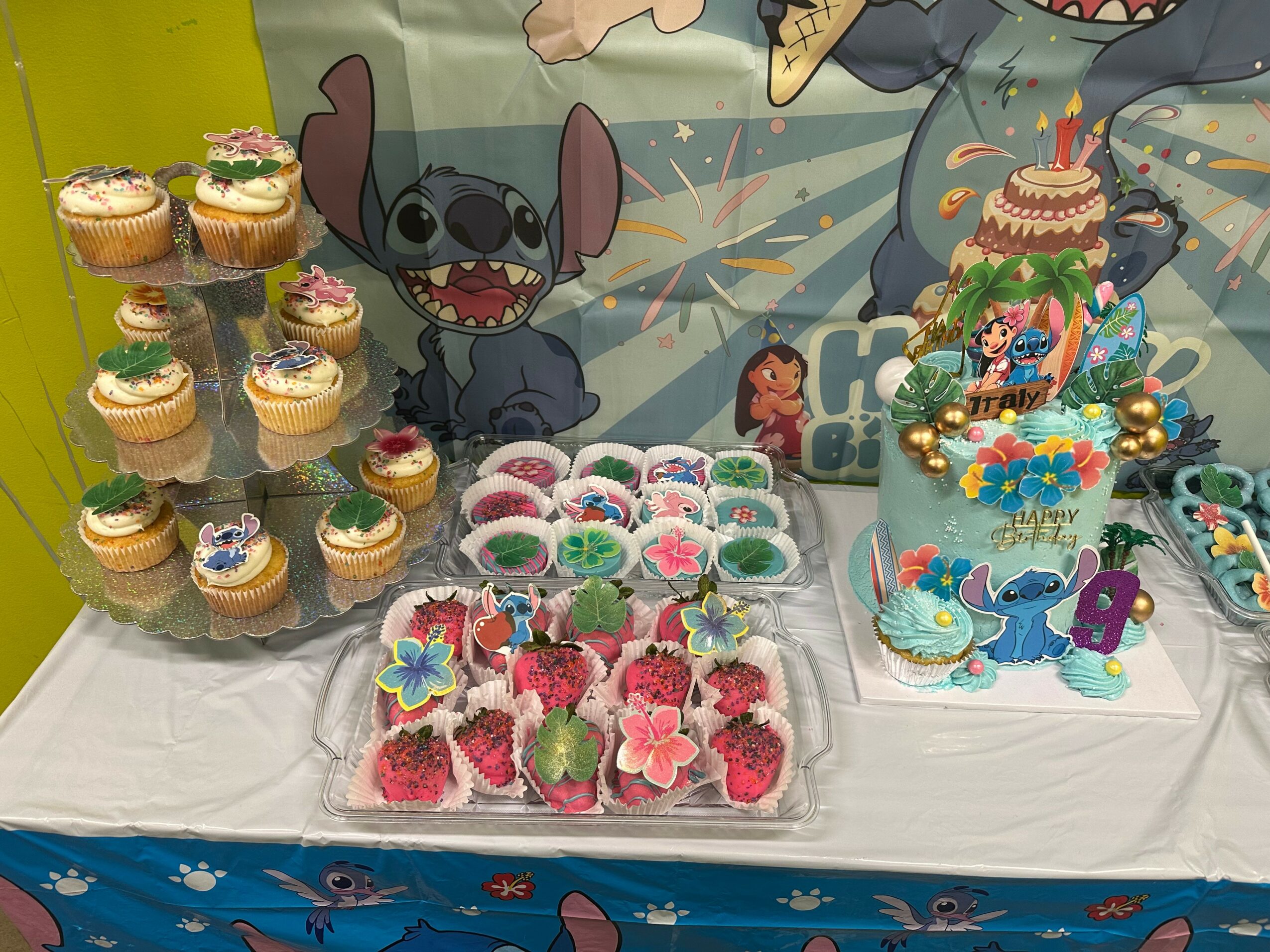 Table with cupcakes, decorated cookies, and a themed cake featuring characters from animated movies, with a colorful backdrop.