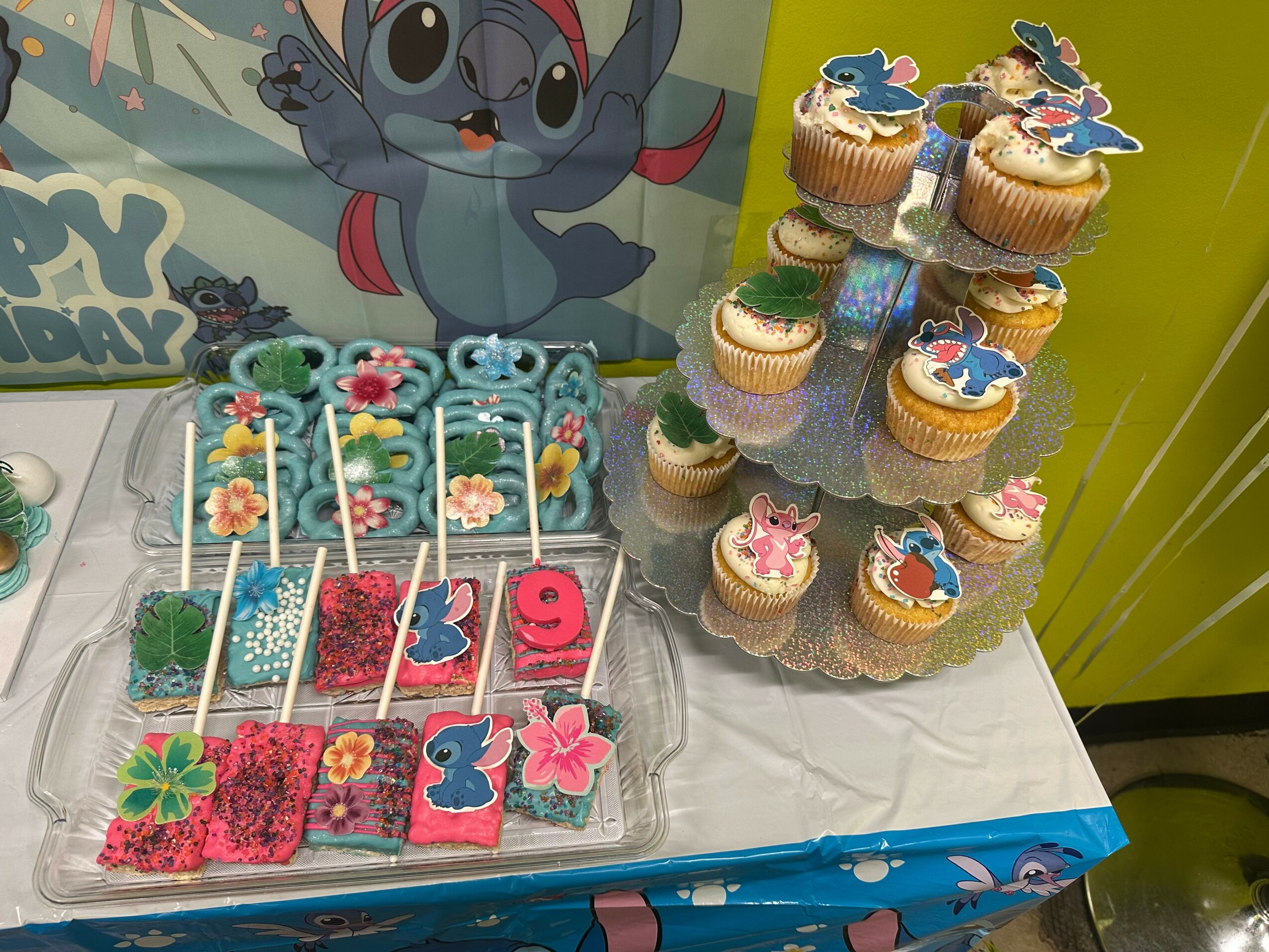 Cupcakes decorated with Stitch from Lilo & Stitch, arranged on a tiered stand, with colorful decorations and a Stitch poster in the background.