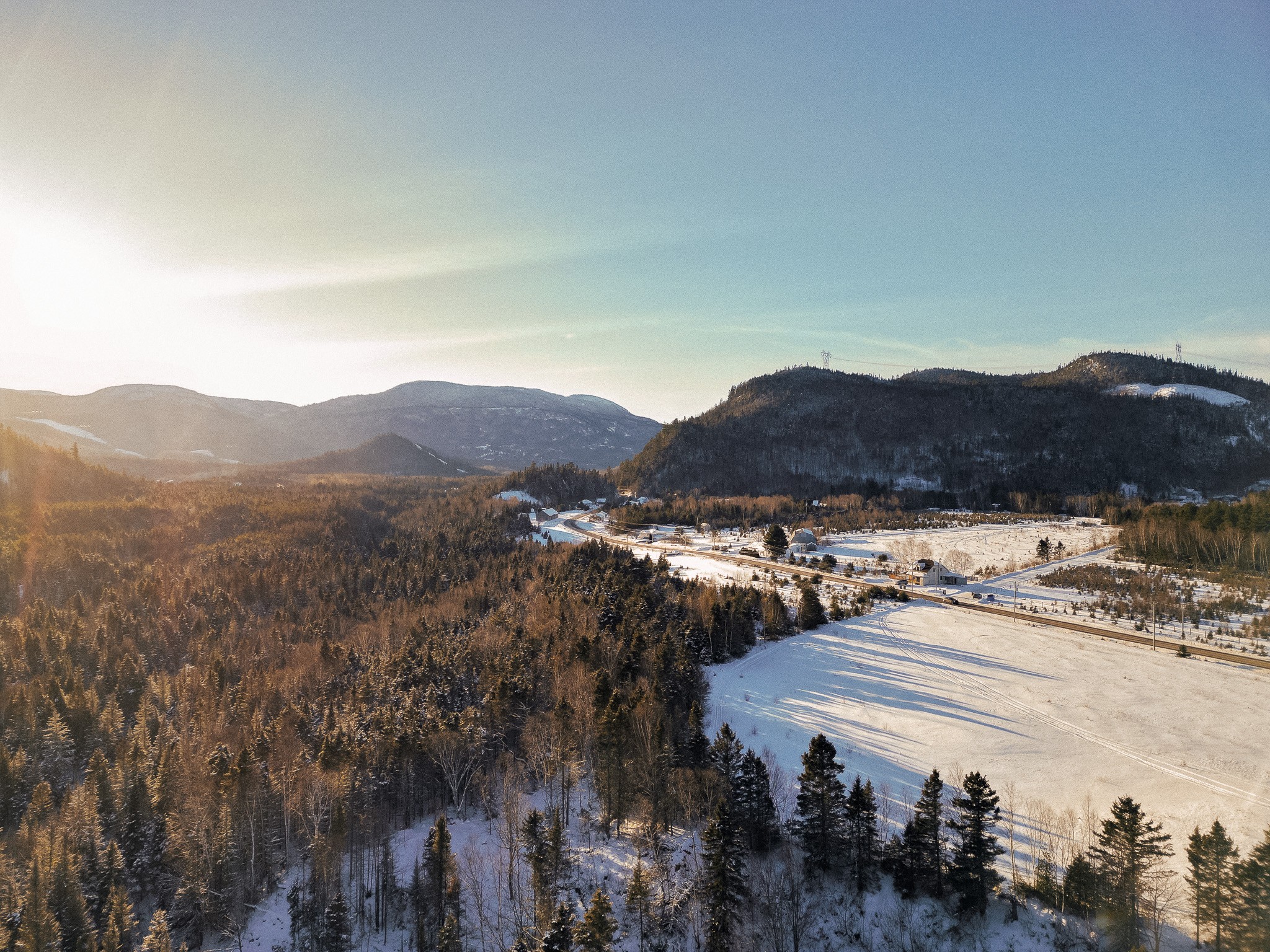 Landscape with mountains, forest, and snow-covered fields under a clear sky, sunlight on the left side.