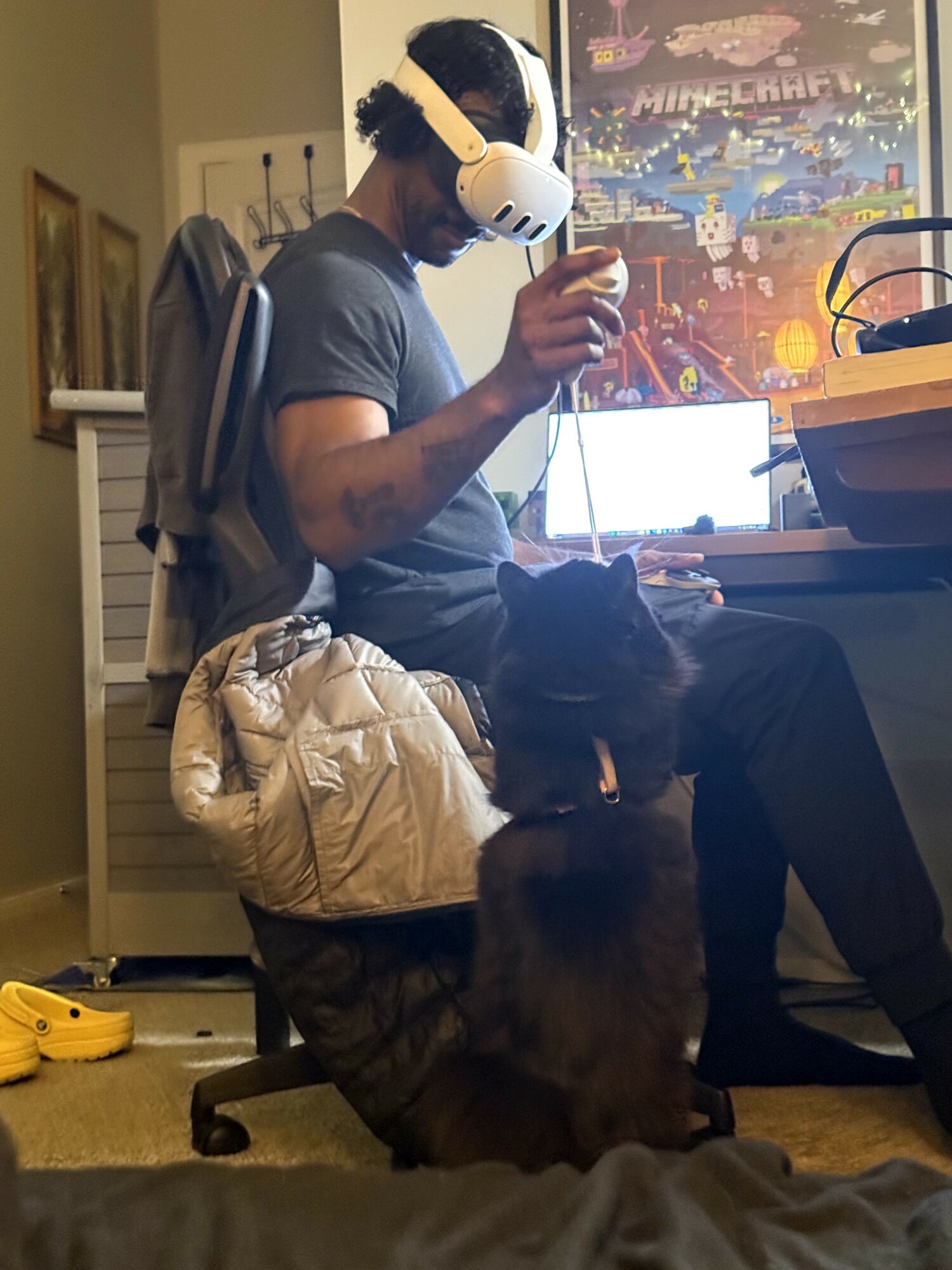 Person wearing a virtual reality headset sitting at a desk with a dog nearby, in a room with colorful wall art.