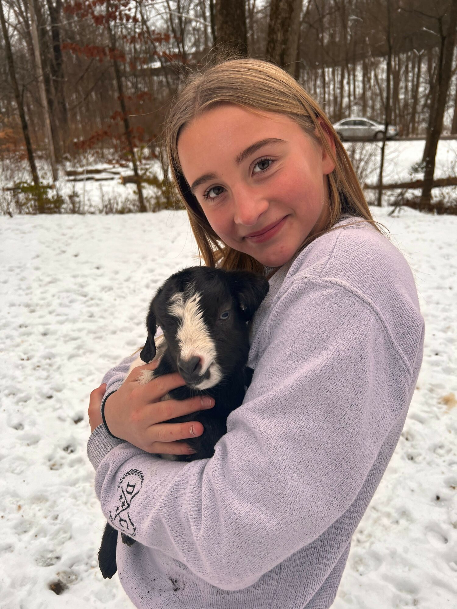 Young girl holding a black and white puppy outdoors in snowy landscape, smiling at camera.