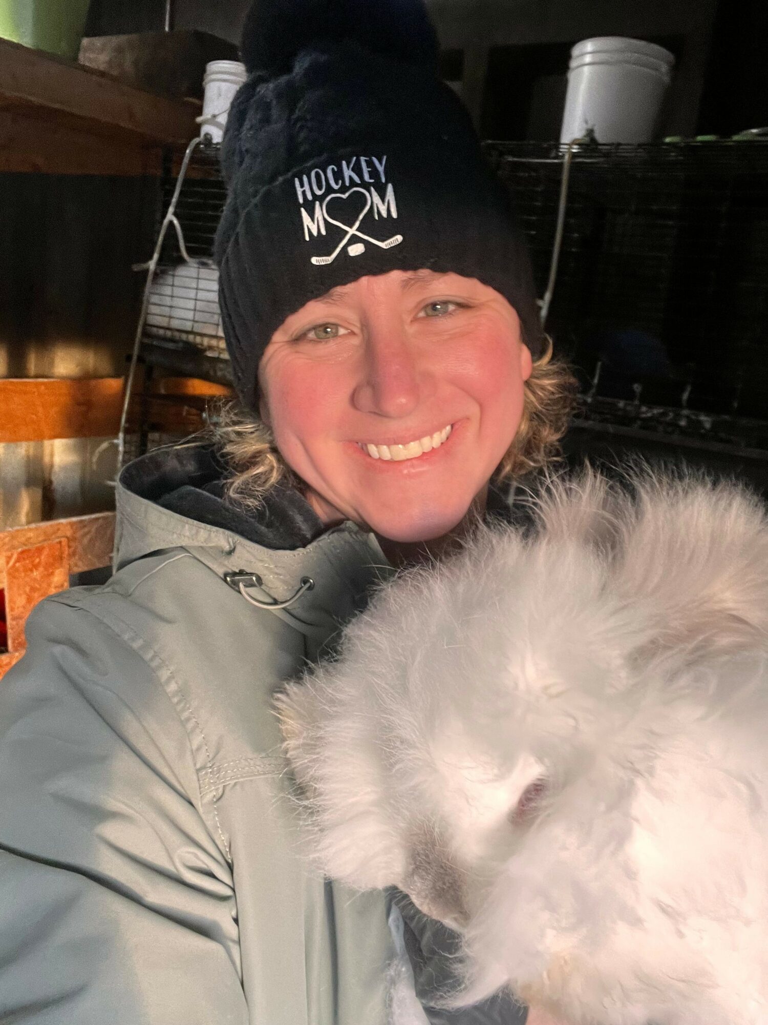 Woman smiling with a dog, both facing the camera, woman wearing a black beanie and light-colored jacket.