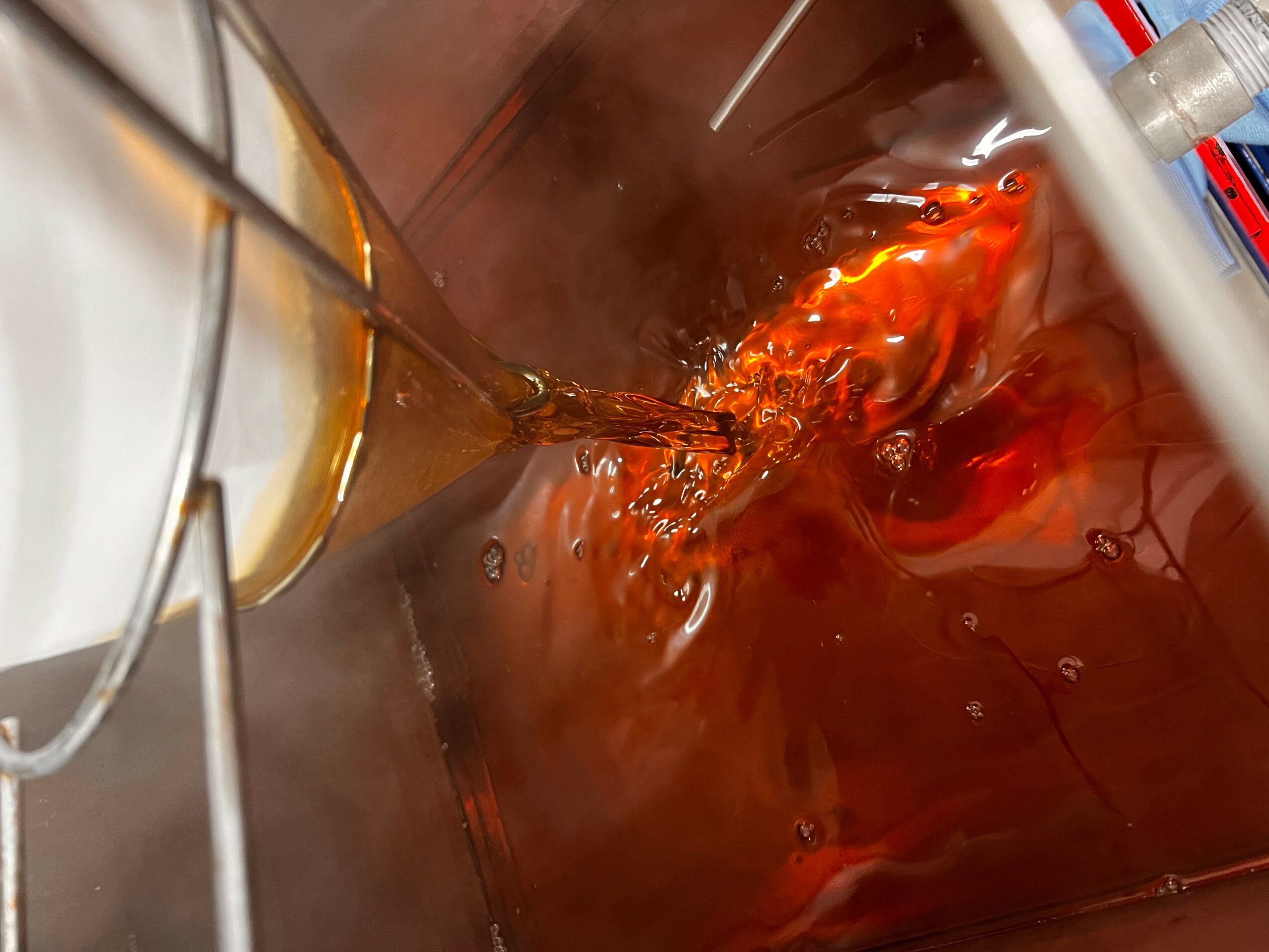 Liquid being poured into a container with steam and bubbles, possibly in a laboratory setting.