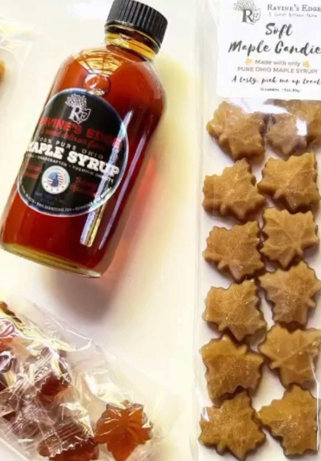 Bottle of maple syrup, maple leaf-shaped cookies, and a partially visible wrapped candy on a white surface.