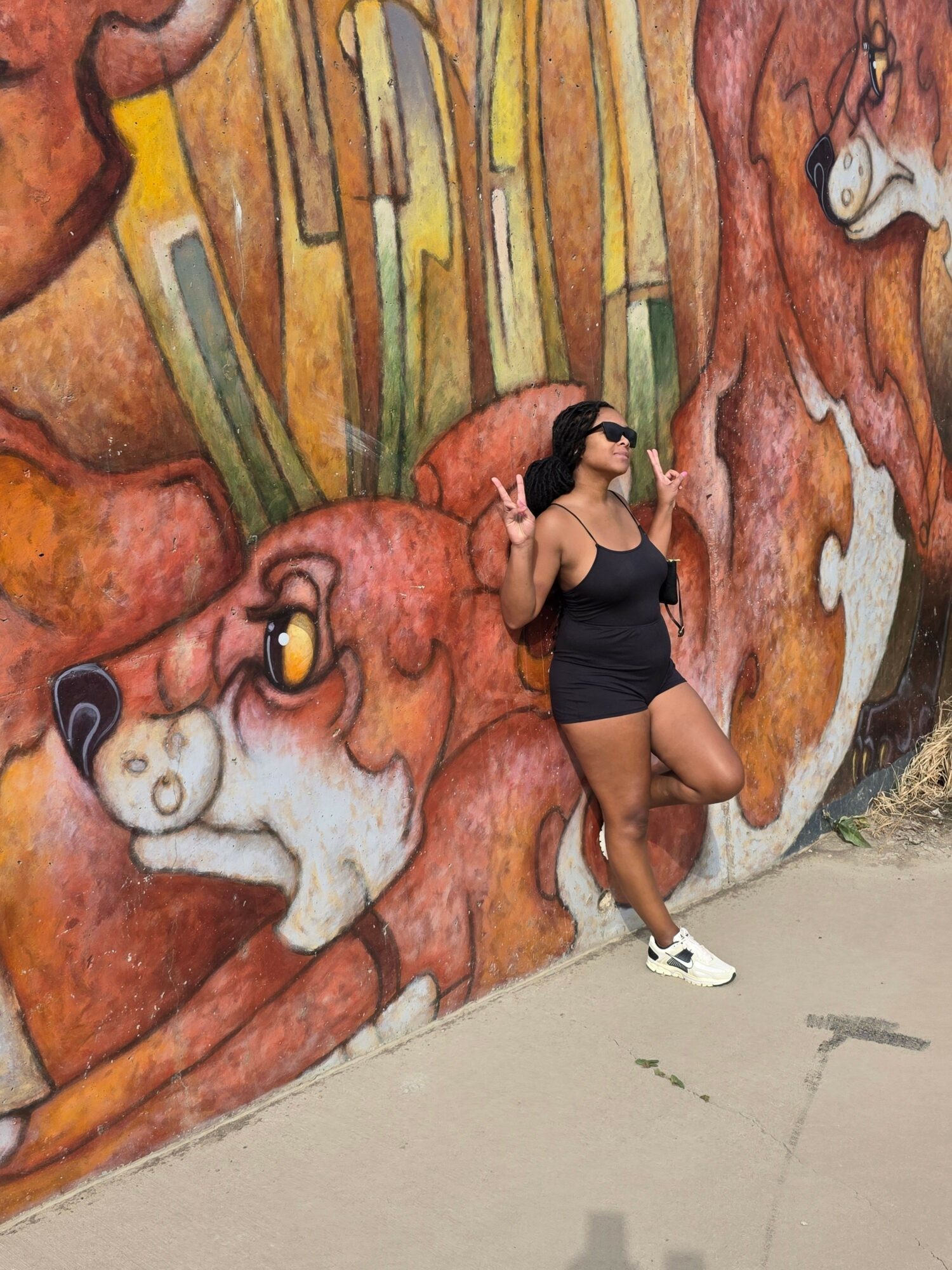 A woman in athletic clothing lying on a colorful mural wall, talking on a phone, with a plain wall in the background.