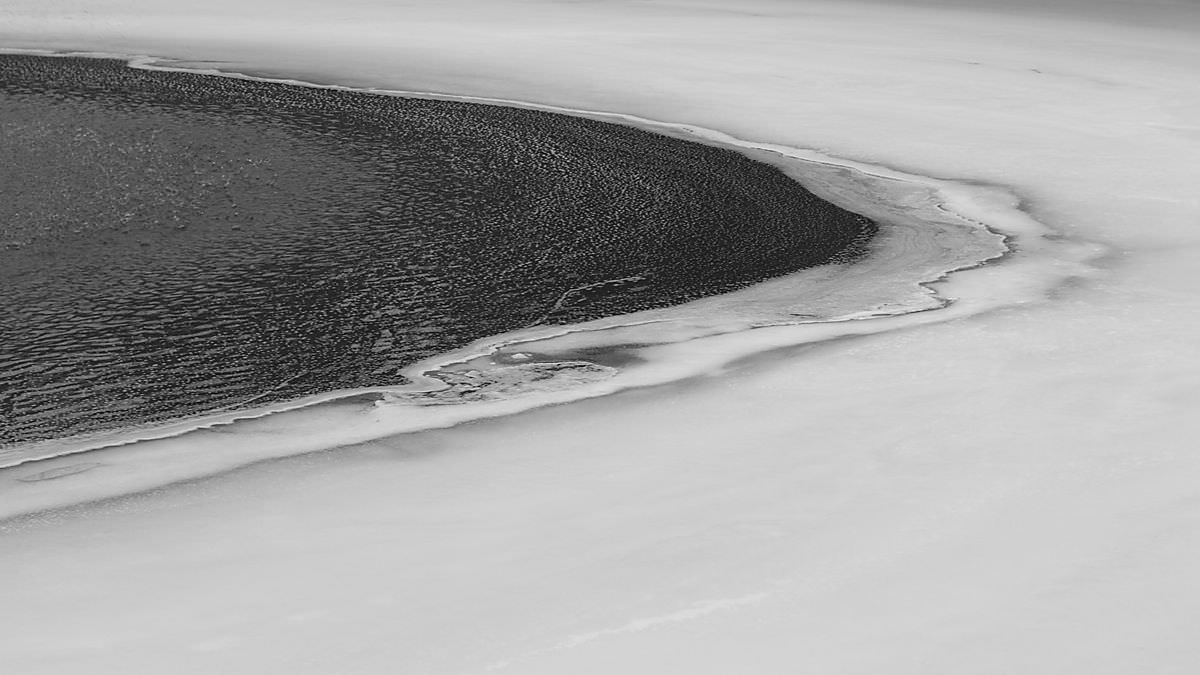 A black sand beach with waves washing onto the shore, with snow or ice covering the sand and water.