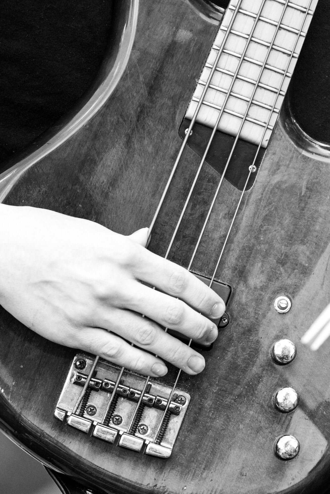 Hand resting on a bass guitar's strings and body, with visible tuning pegs and control knobs.