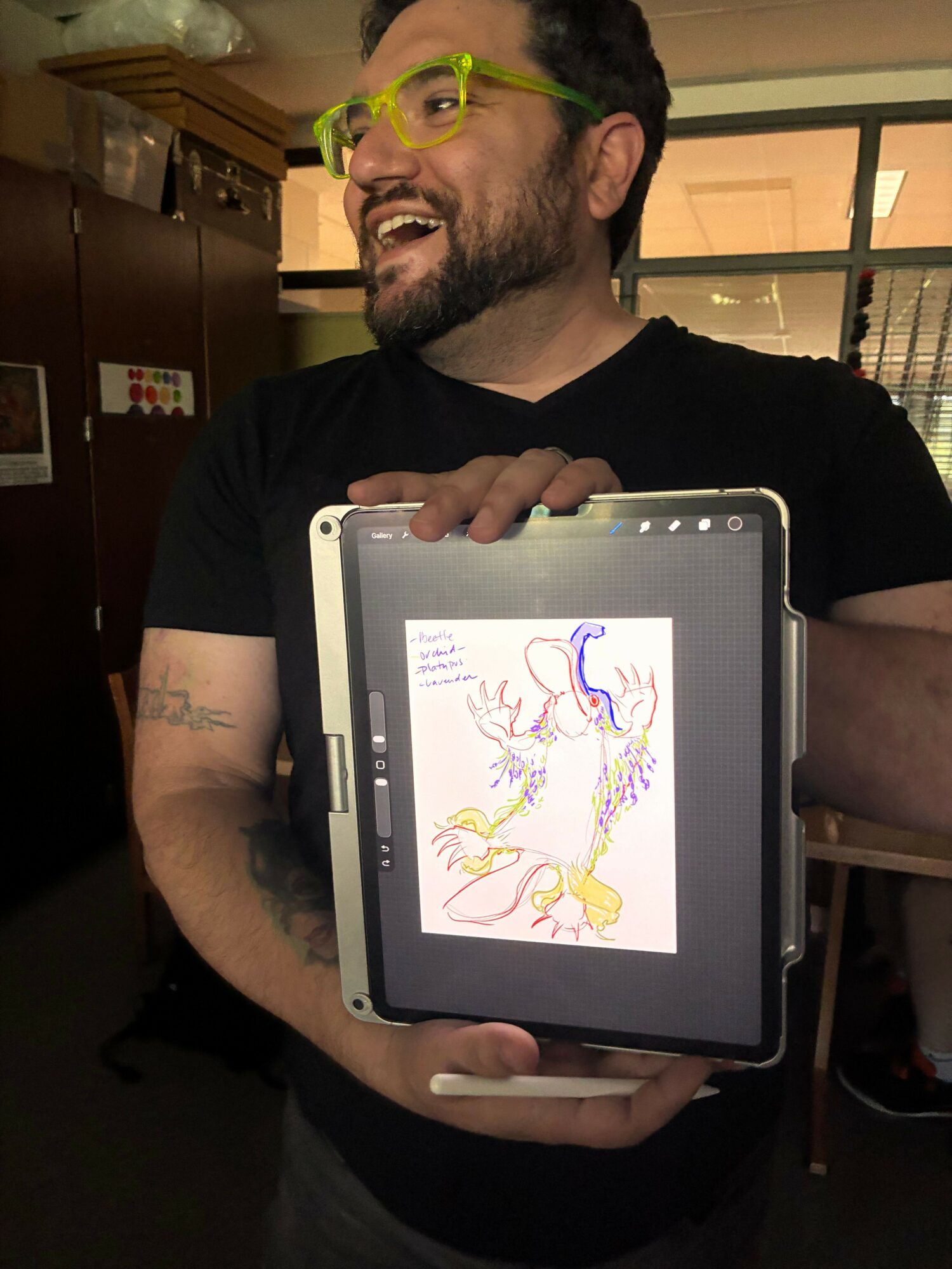 Person with glasses holding a tablet displaying a colorful drawing of a unicorn with a rainbow mane and tail.
