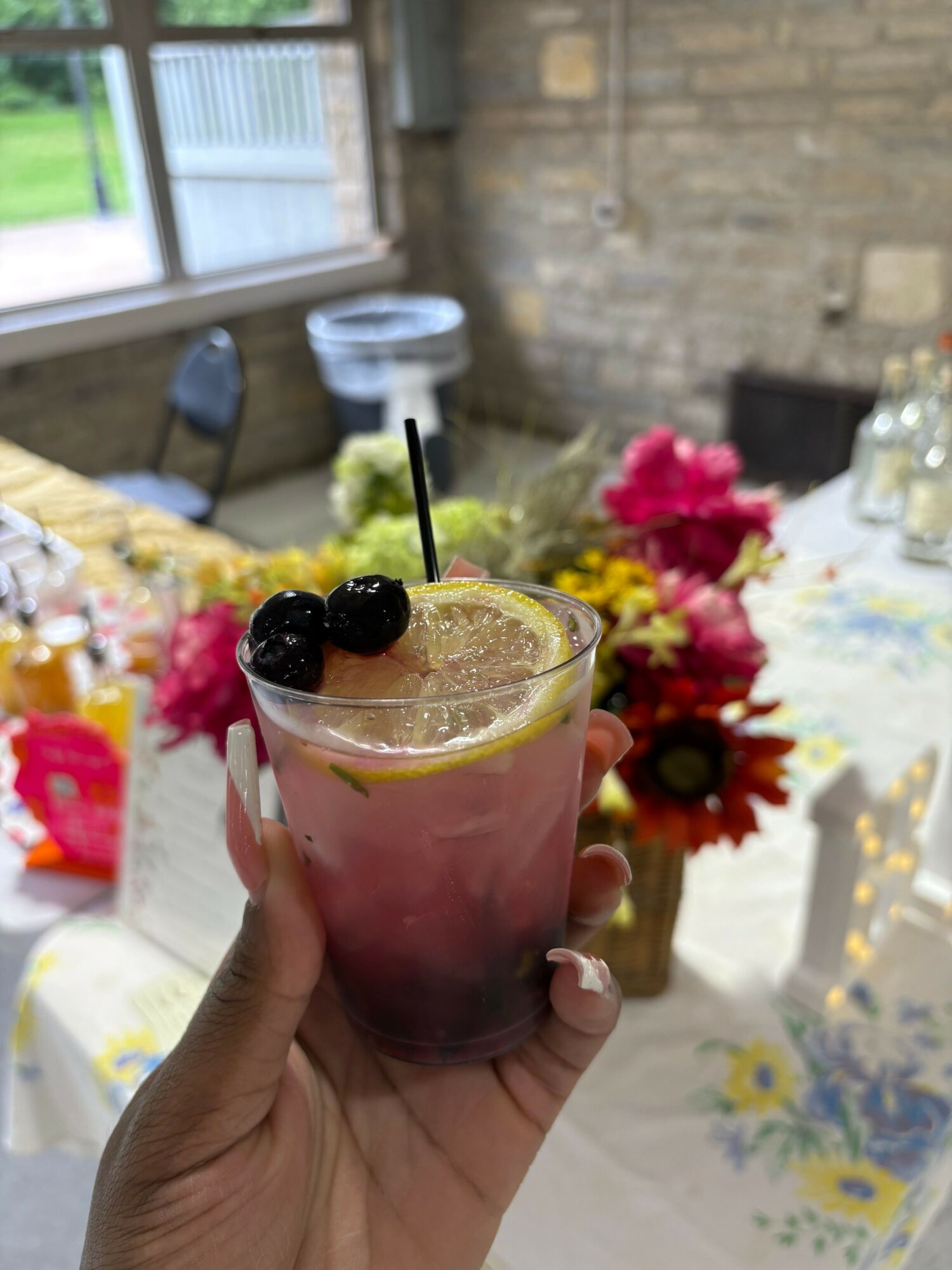 Hand holding a glass with a pink drink, blackberries, and a lime wedge, with a floral background.