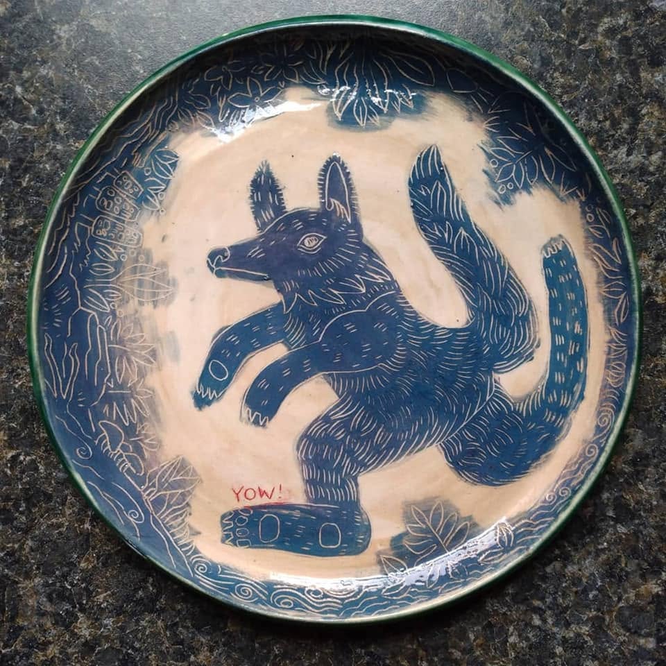 Decorative round plate with a blue fox illustration, surrounded by floral patterns, on a dark surface.
