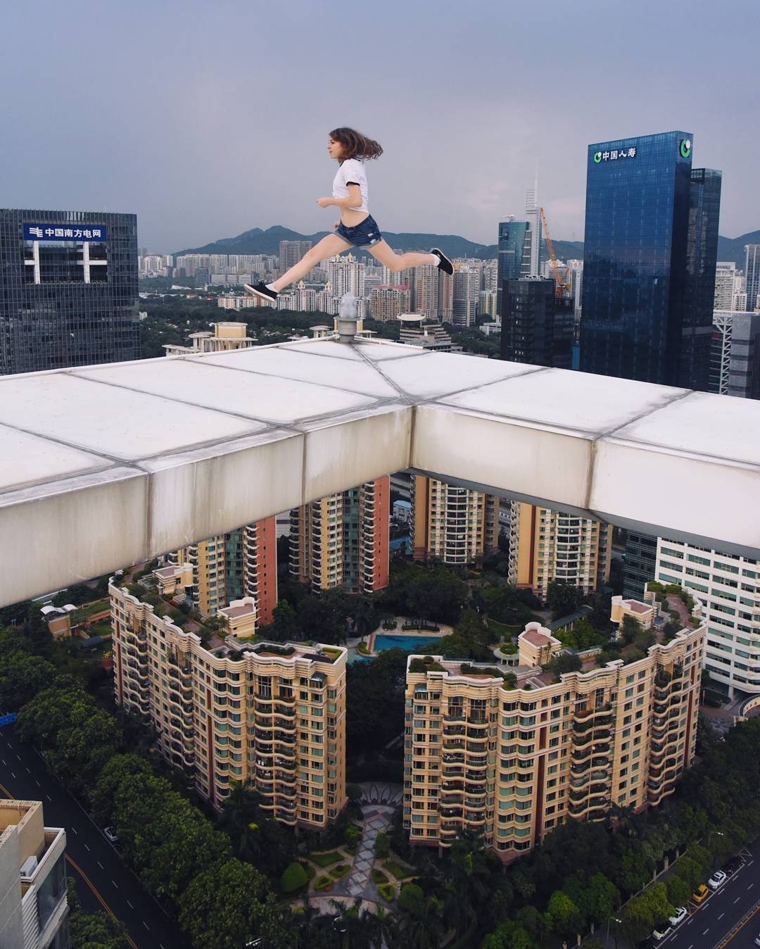 A person is mid-air jumping between two buildings in a cityscape, with tall buildings and a cloudy sky in the background.