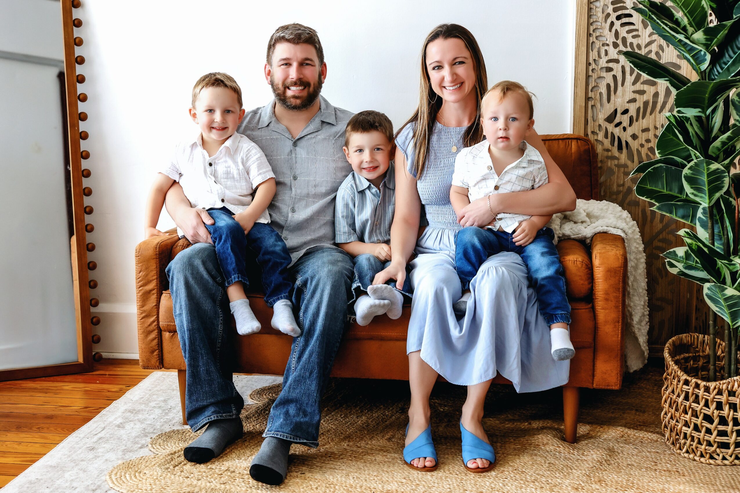 Family of five sitting on a sofa in a living room, smiling, with plants and decorative items around.