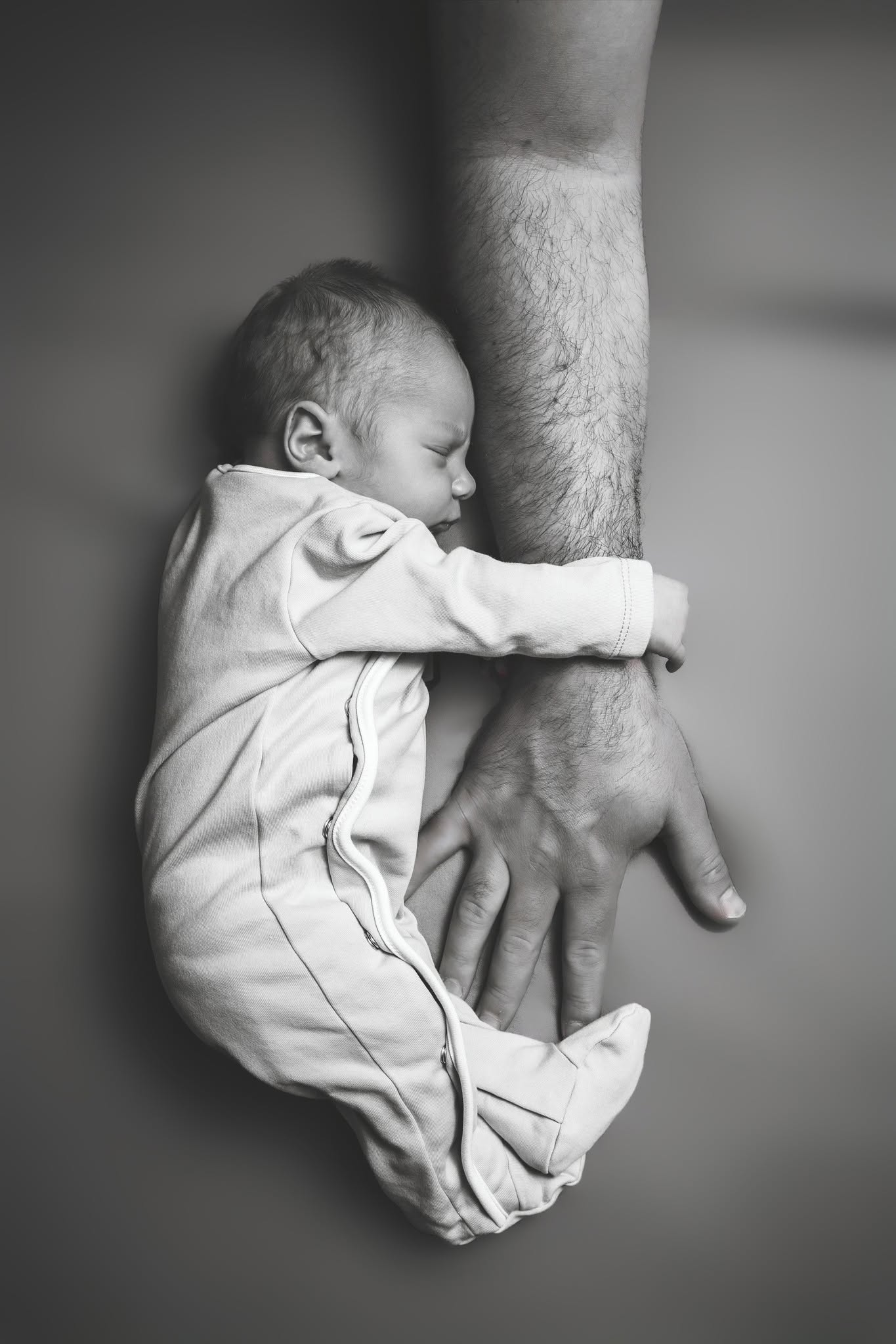 Baby sleeping with head resting on an adult's arm, lying on a flat surface, black and white photo.