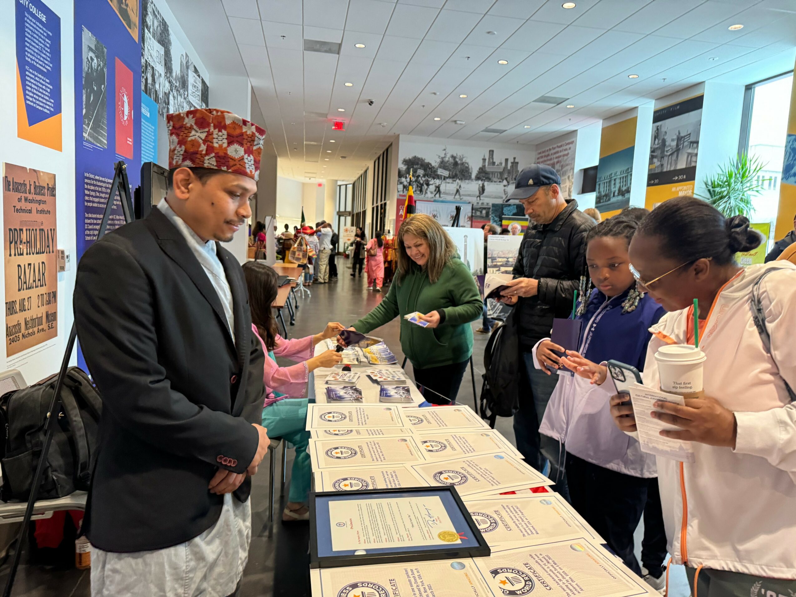 People gather around a table with informational materials in a brightly lit indoor space, engaging in conversation and reading documents.