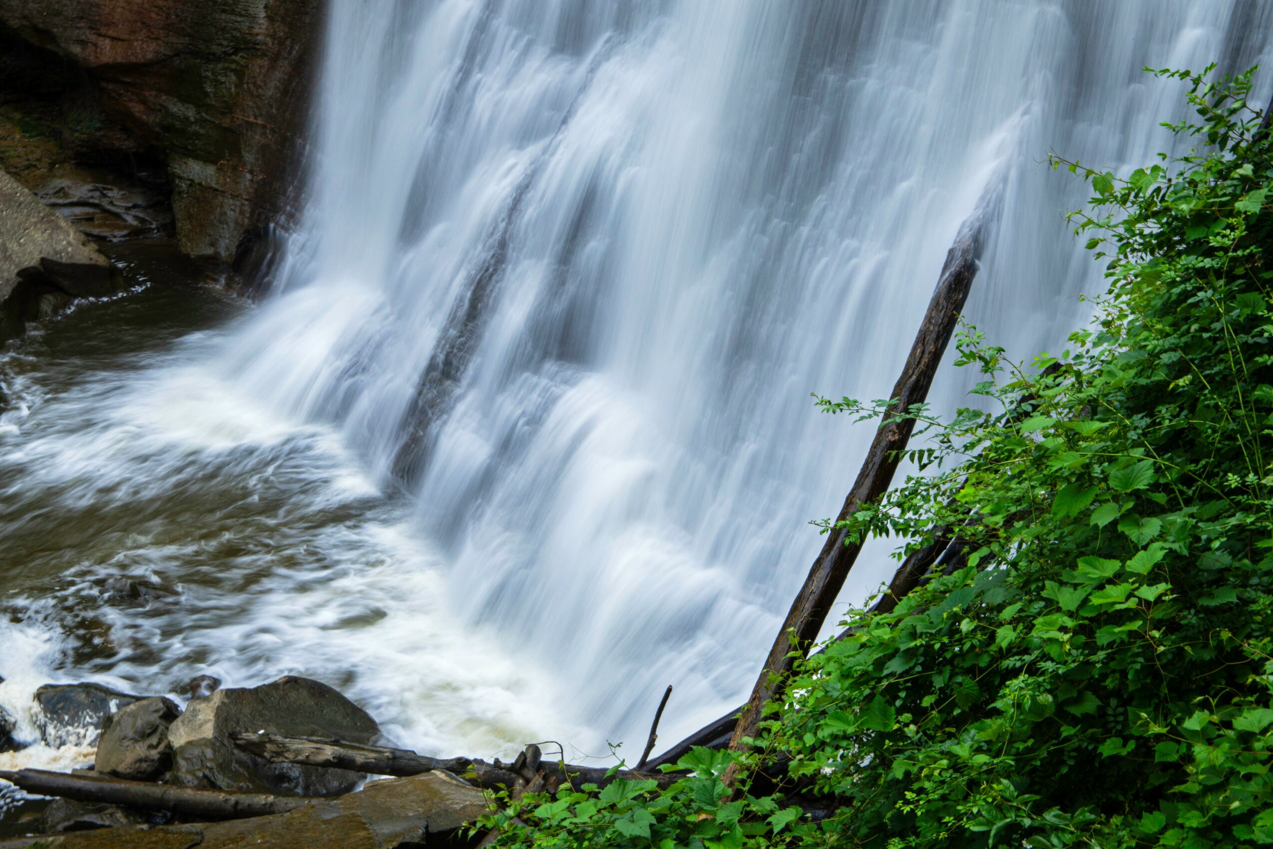 Waterfall flowing over rocks with green foliage on the right side, water splashing at the bottom.