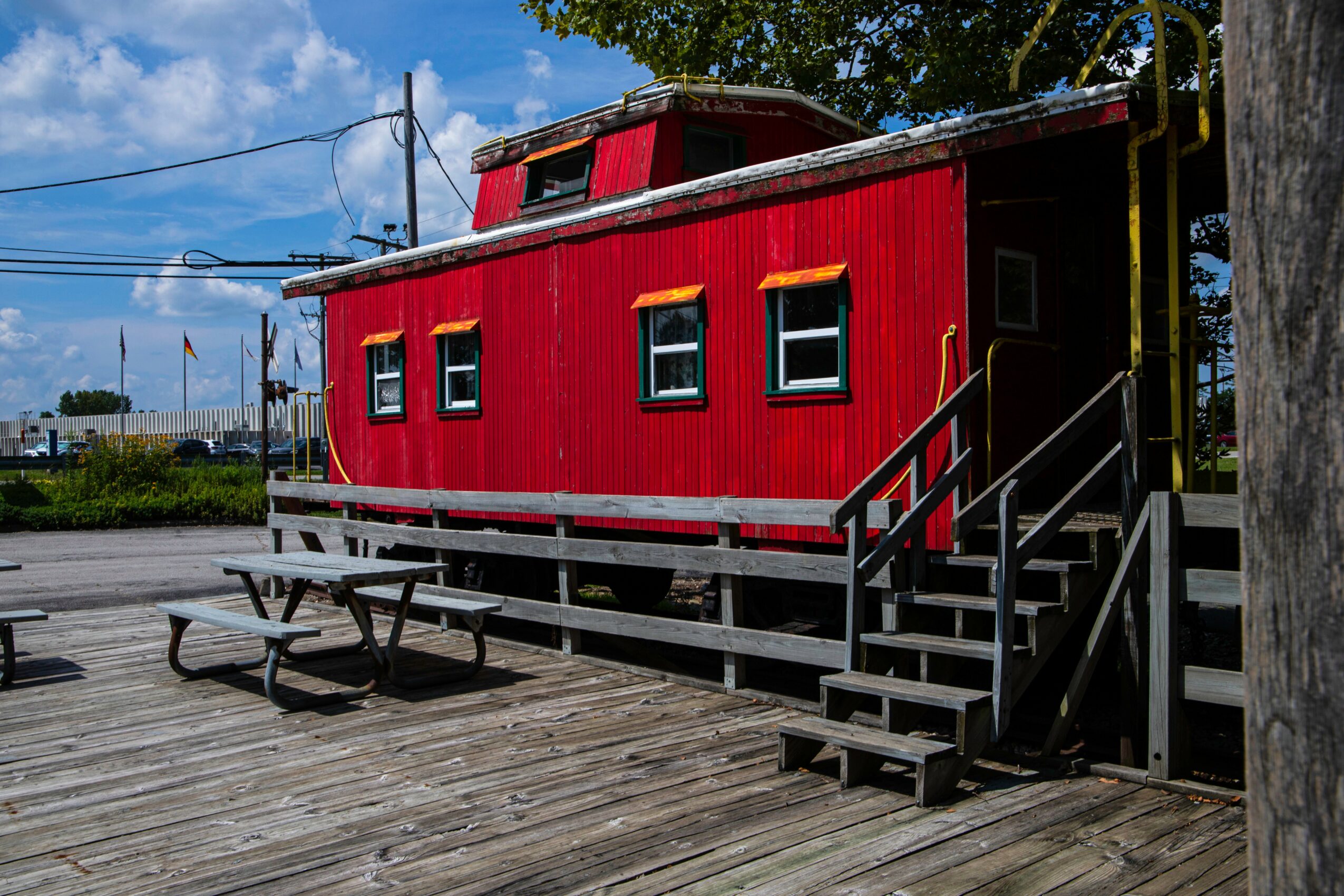 Red building with windows, stairs, and a deck, outdoors with trees and sky in background.