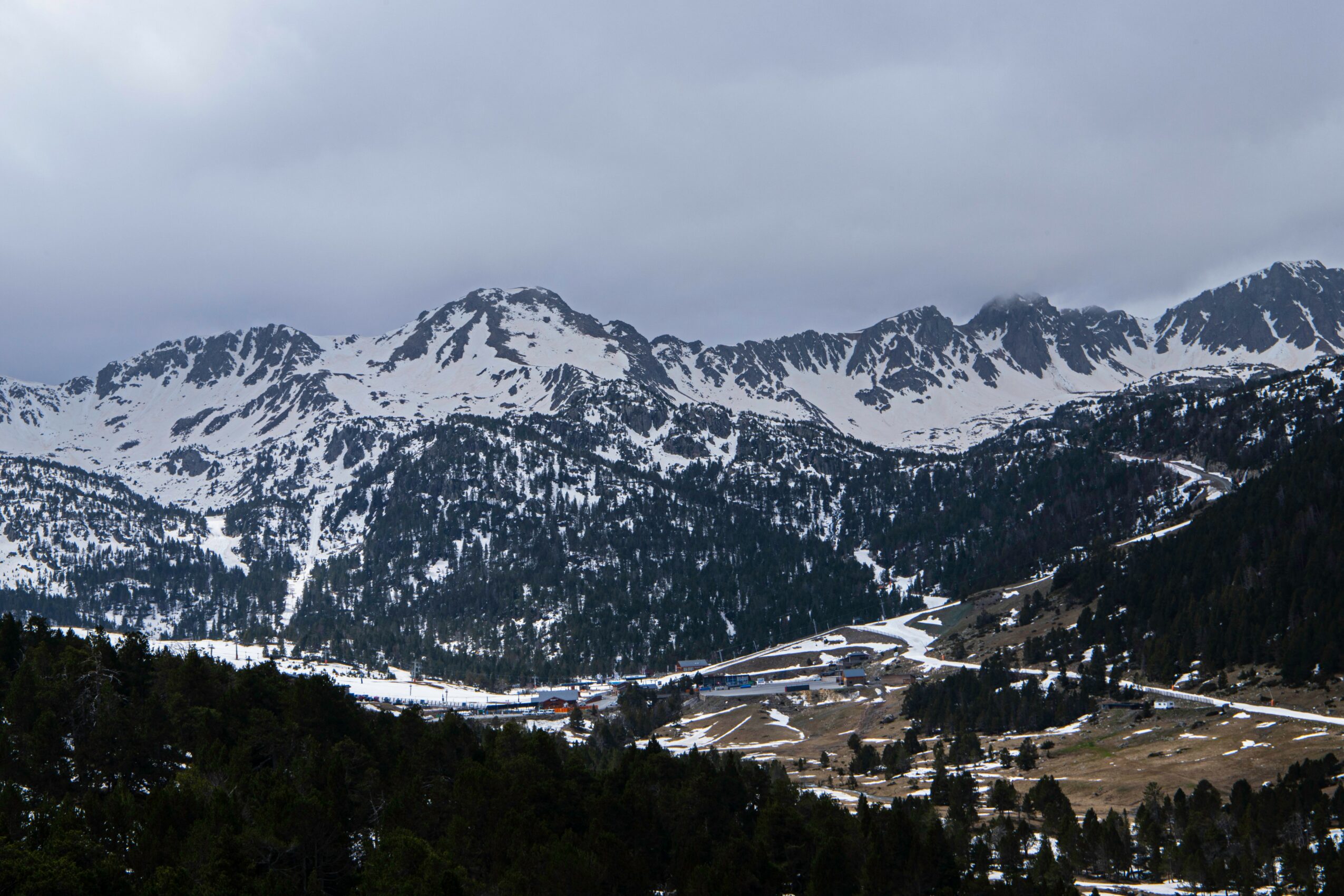 Snow-covered mountain range under cloudy sky with forested slopes and a valley below, no people visible.